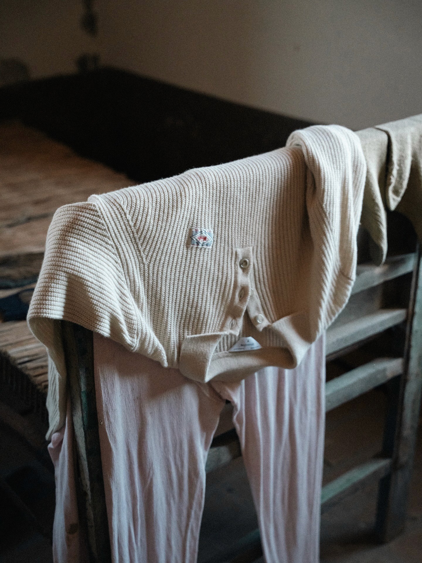 Nature morte d'un pull colpolo blanc posé sur une rambarde dans le lookbook de la marque Italienne masculine Wooden Storepour la saison FW25