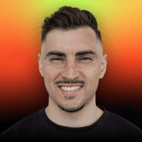 A woman with short curly hair wearing a black t-shirt looks into the camera.