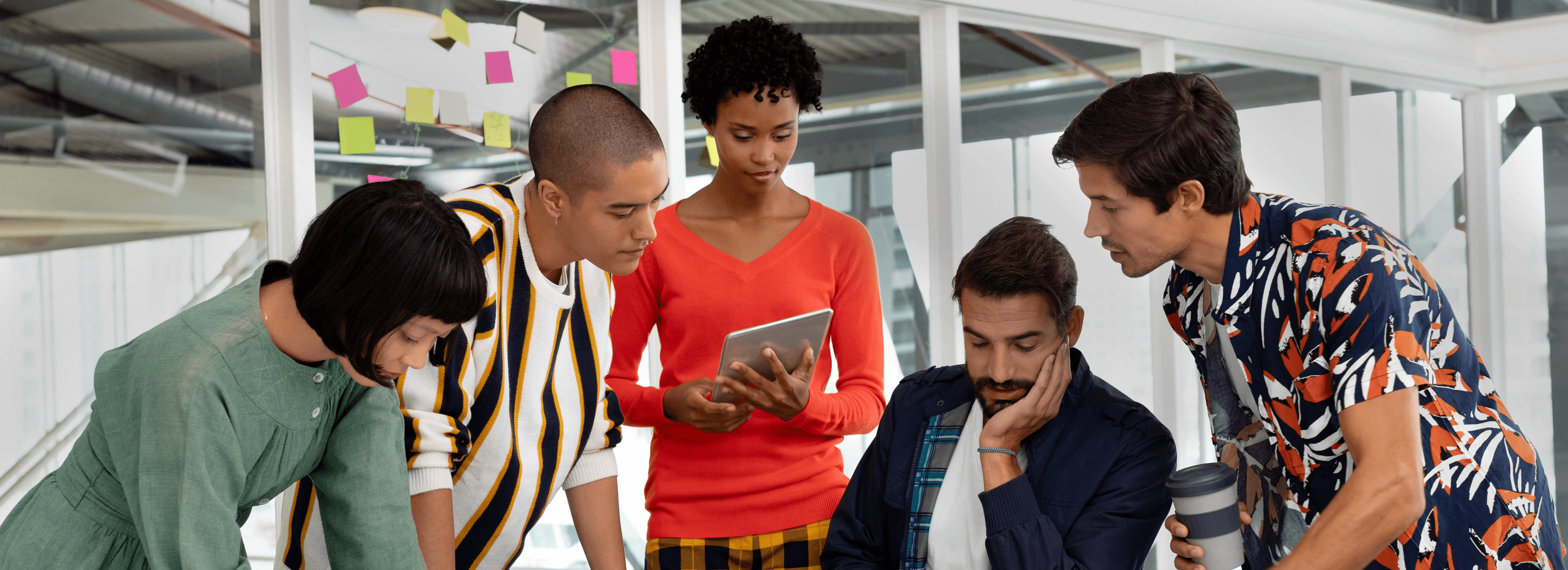 Team of five young coworkers collaborating around a tablet in a modern office.