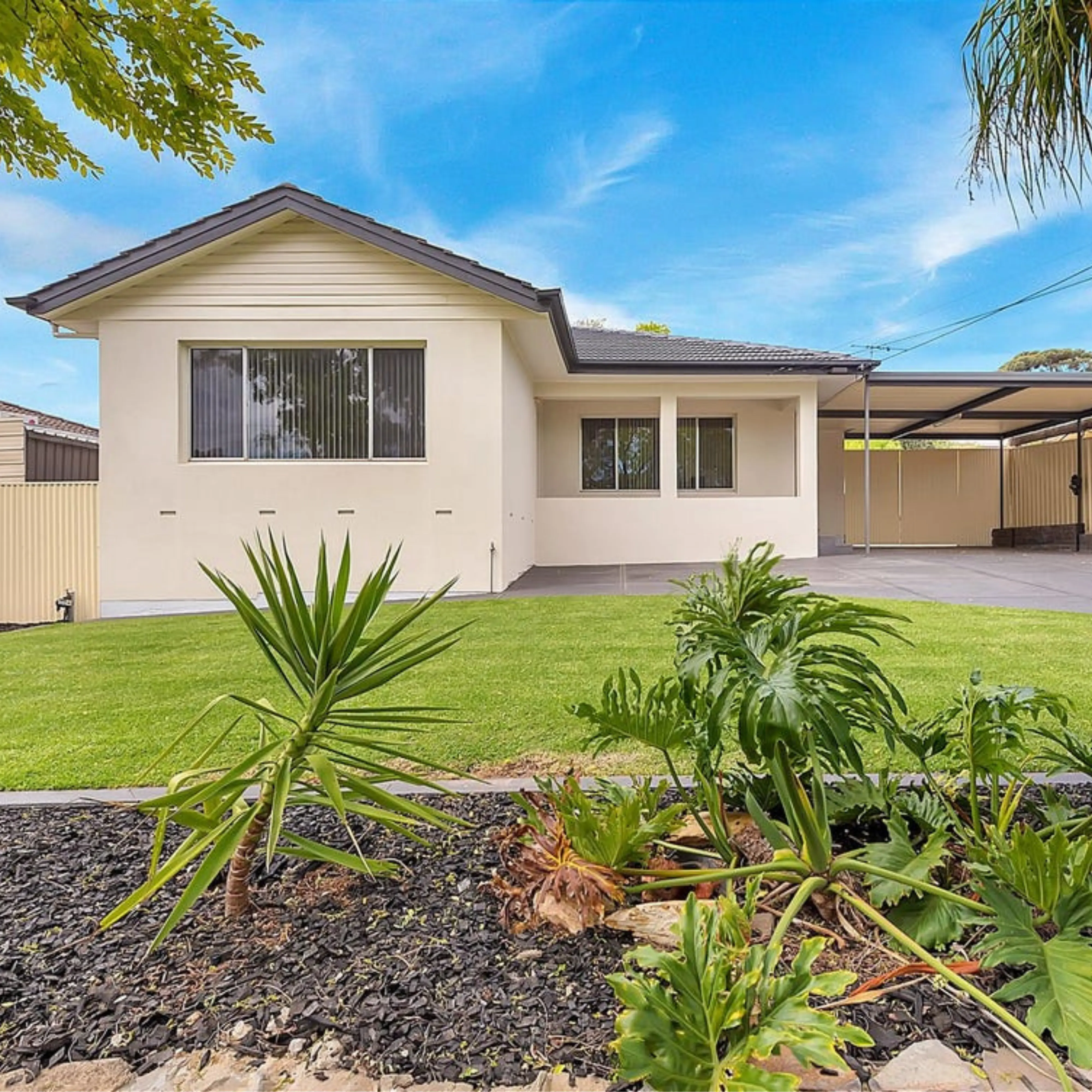 Cream house with carport, lawn, and tropical plants