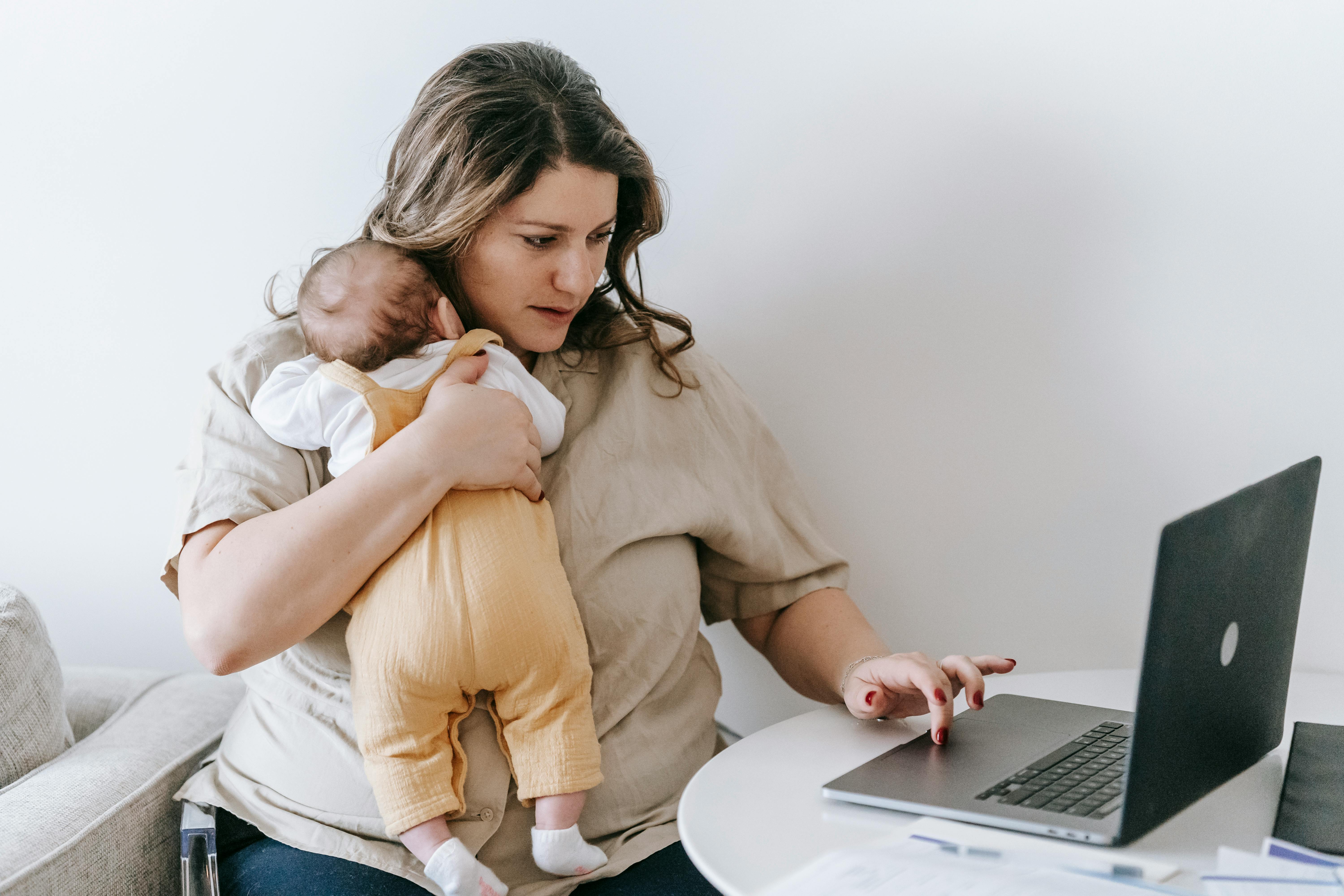 Donna che tiene in braccio il proprio bambino mentre lavora al computer, rappresentazione di equilibrio tra lavoro e vita familiare.