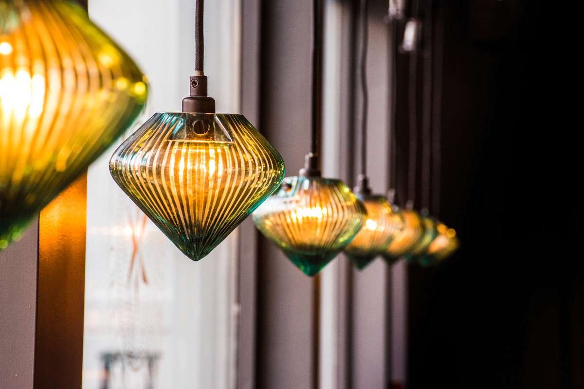 A row of green and yellow ribbed glass pendant lamps hanging in a line along an indoor ceiling.