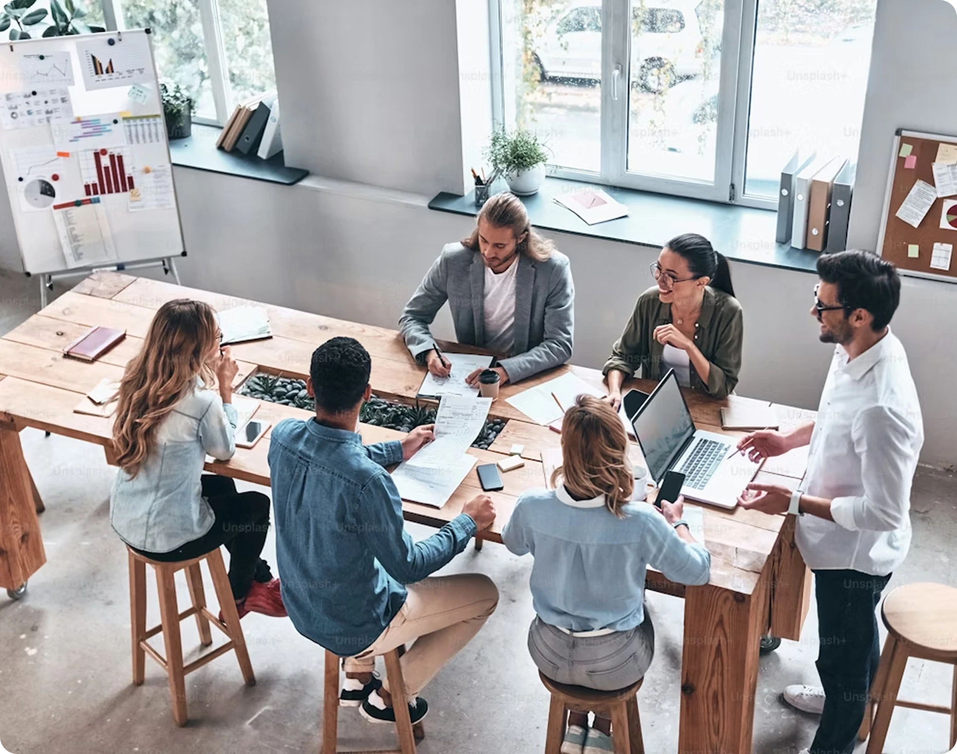 Overhead view of six diverse professionals collaborating around a wooden table in modern office