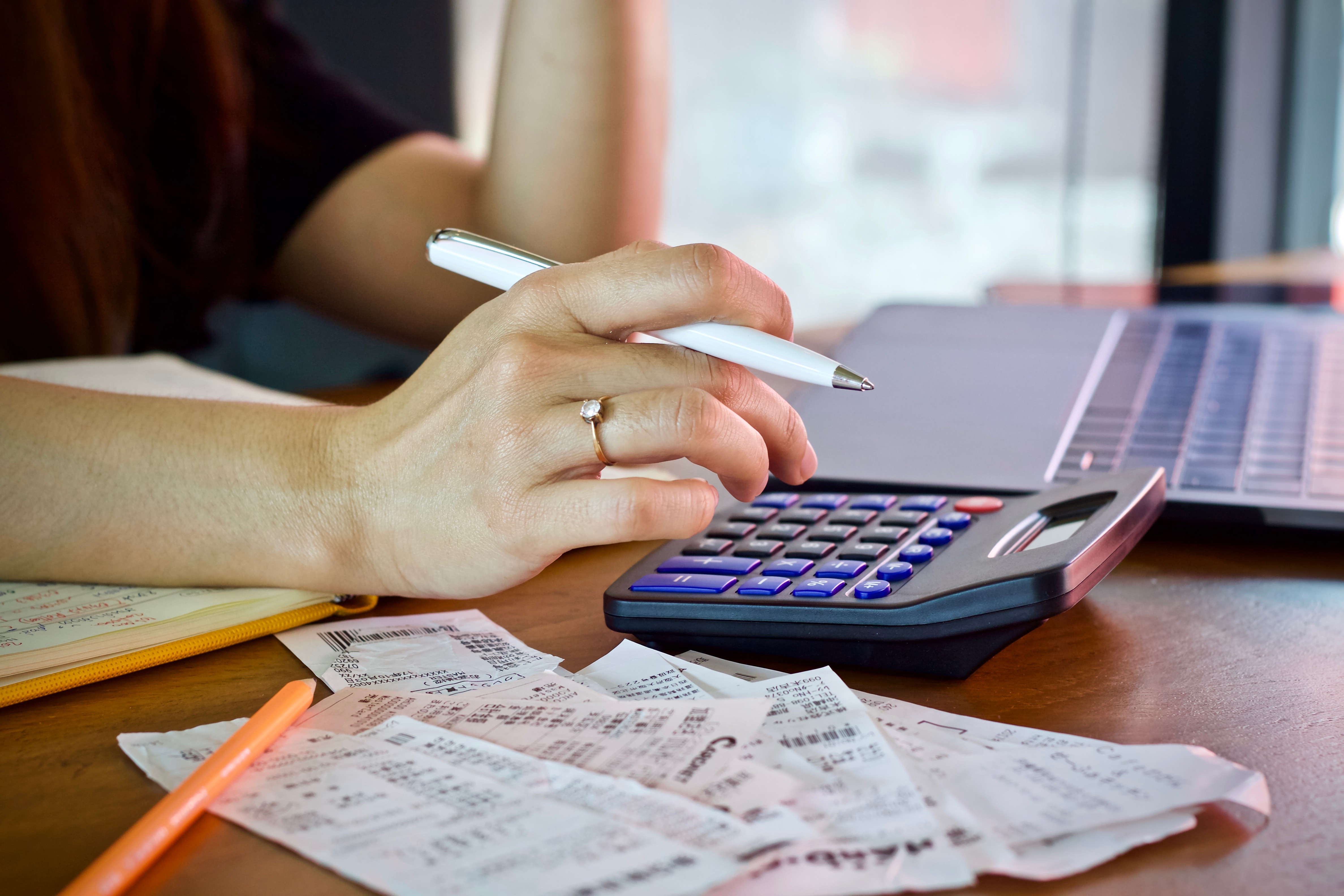 Woman reviewing bills and using a calculator at a desk, representing the process of budgeting and managing costs while producing explainer videos.