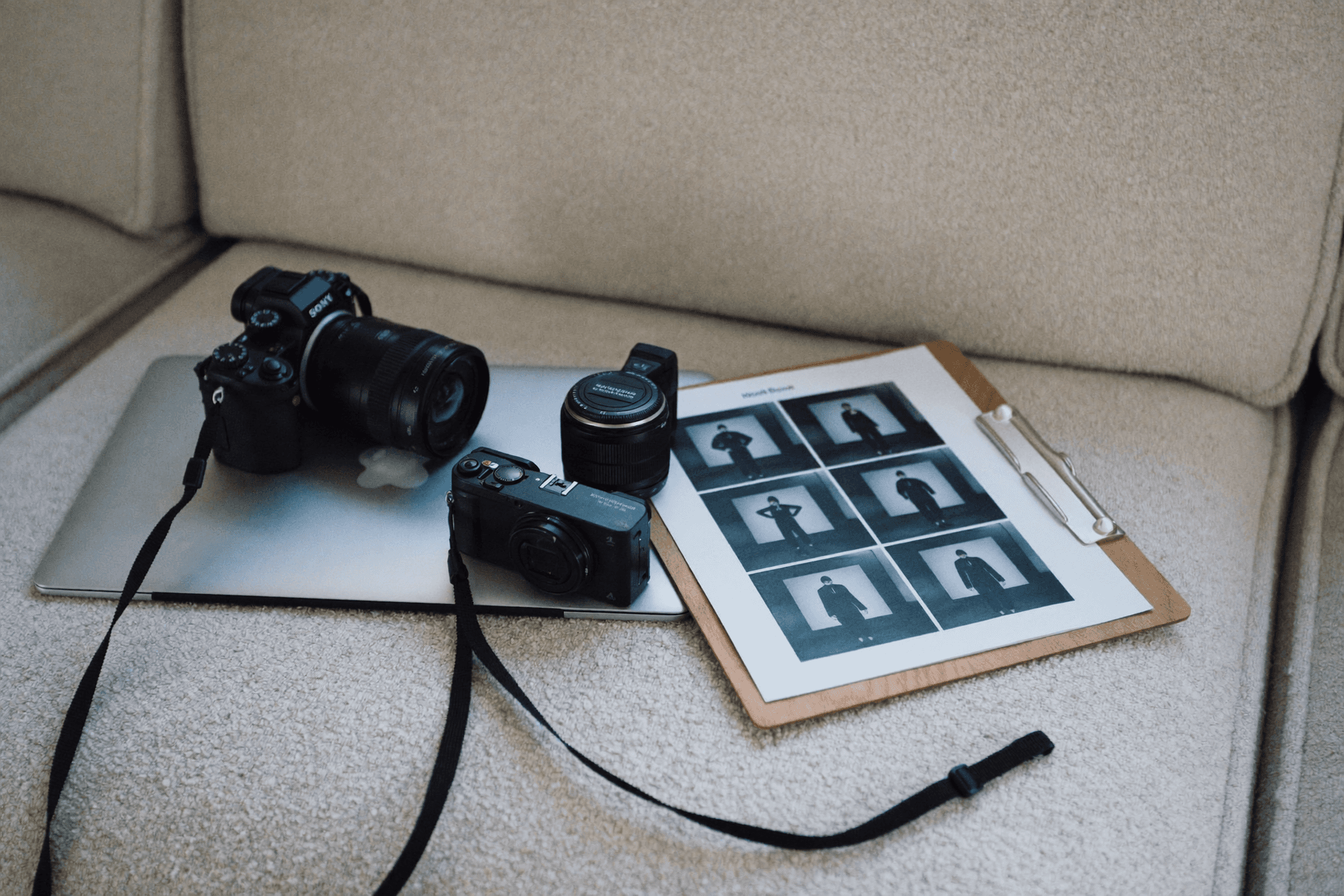 A woman in a teal dress sits in a dimly lit room, focused on her smartphone. A laptop and notepad are on the glass table, suggesting a working environment.
