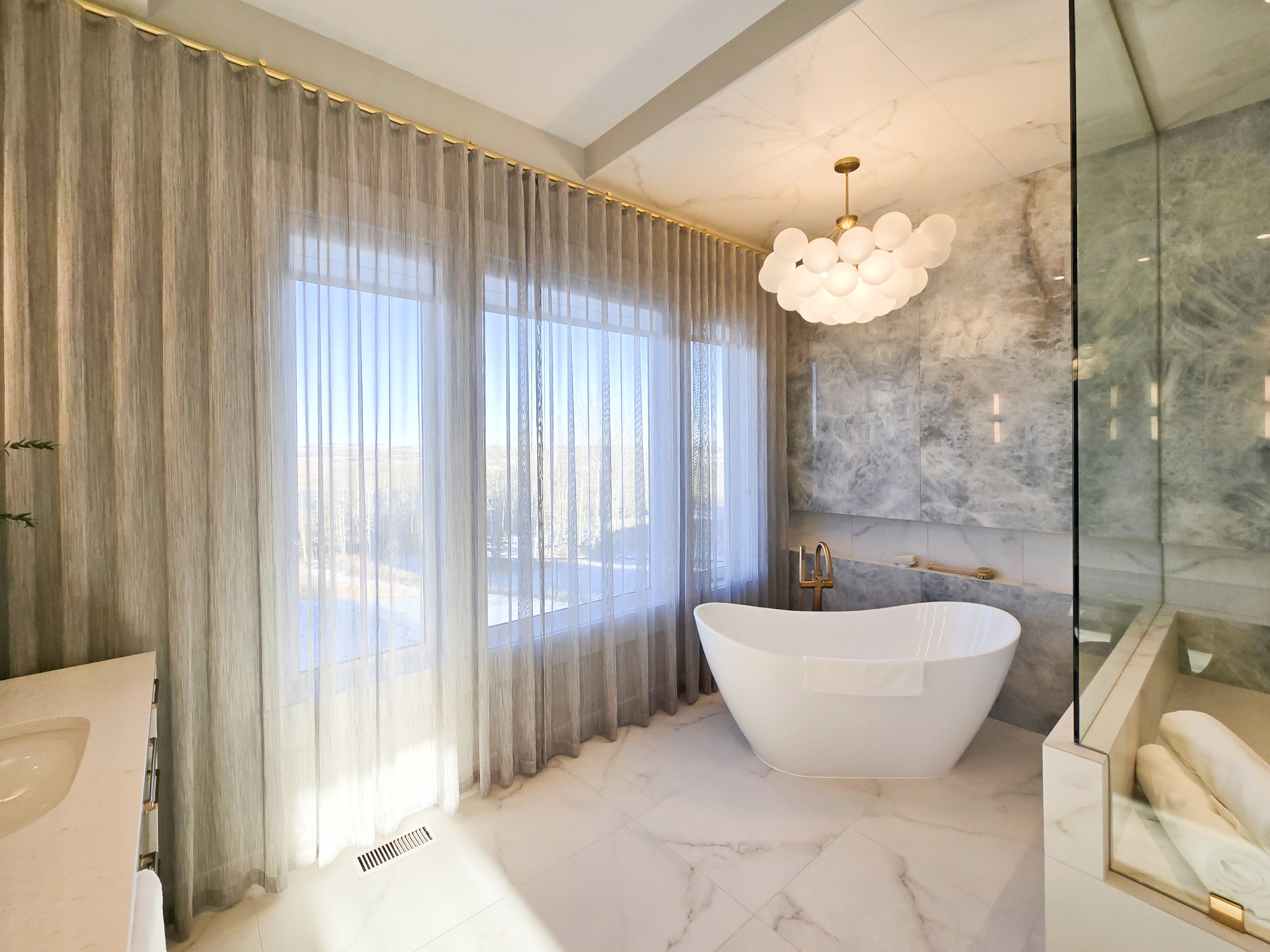 Image of Luxurious primary ensuites with freestanding tub, marble walls, and modern window coverings by KHD Homes.