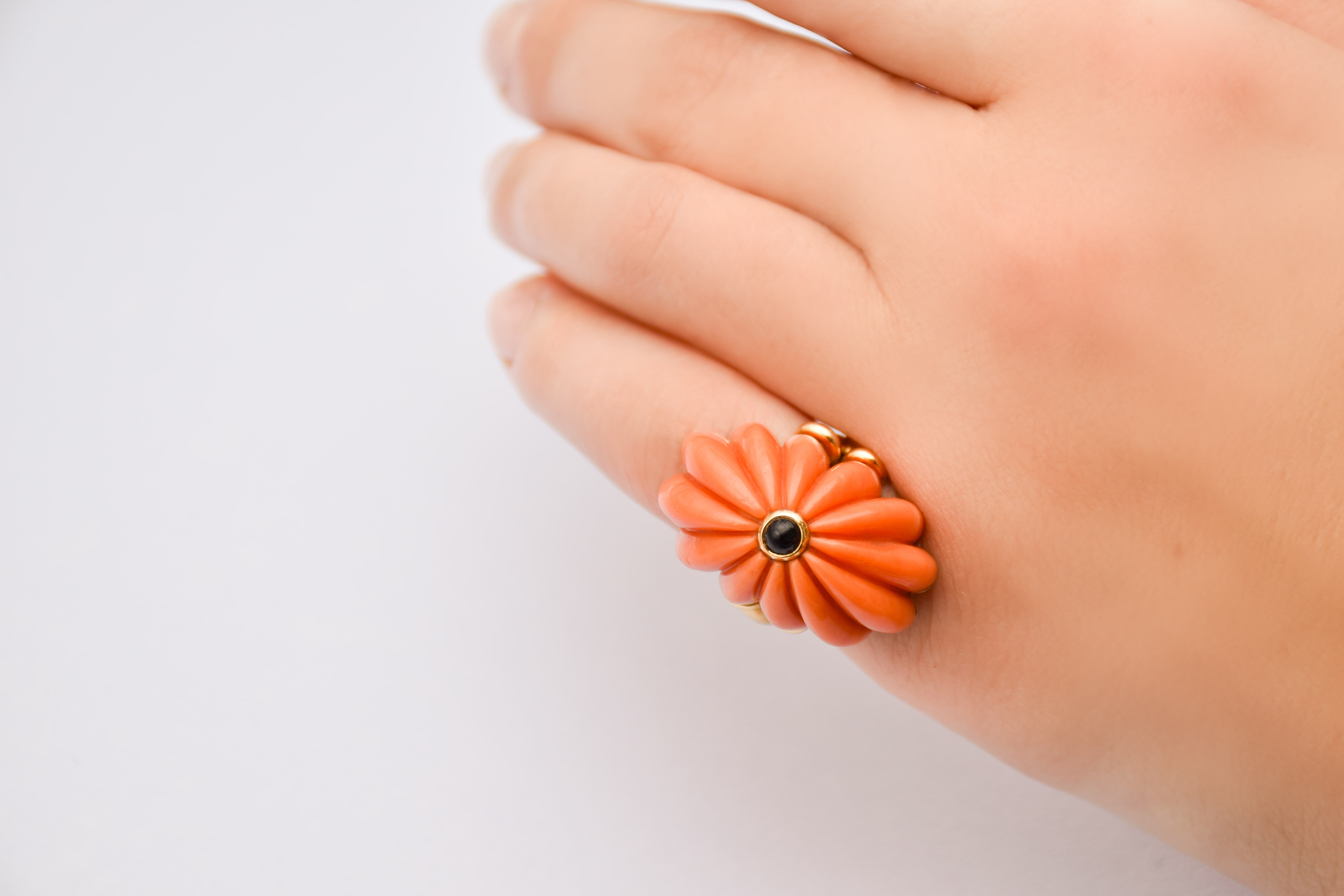 Gros plan vue portée d'une bague Chaumet en corail en forme de fleur avec un petit cabochon d'onyx sur le dessus 