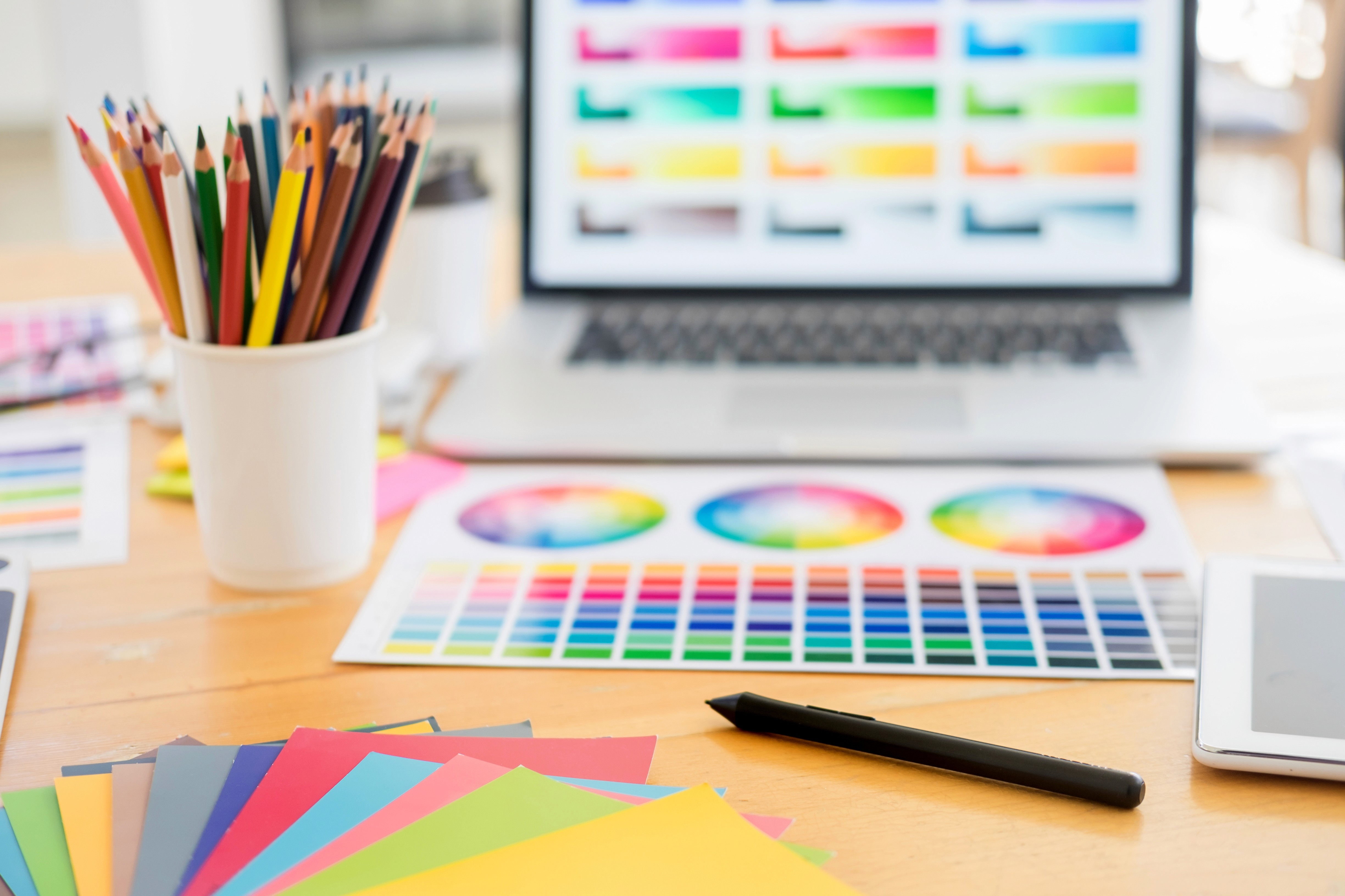 Creative designer workspace with color swatches, color wheel charts, colored pencils, and laptop — graphic design and color theory concept workign on portfolio.