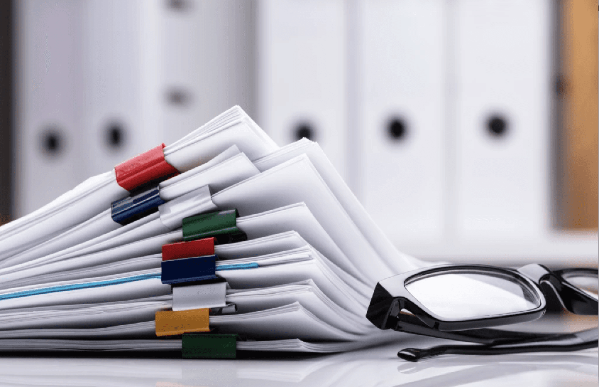 stacked documents with colorful paperclips and eyeglasses