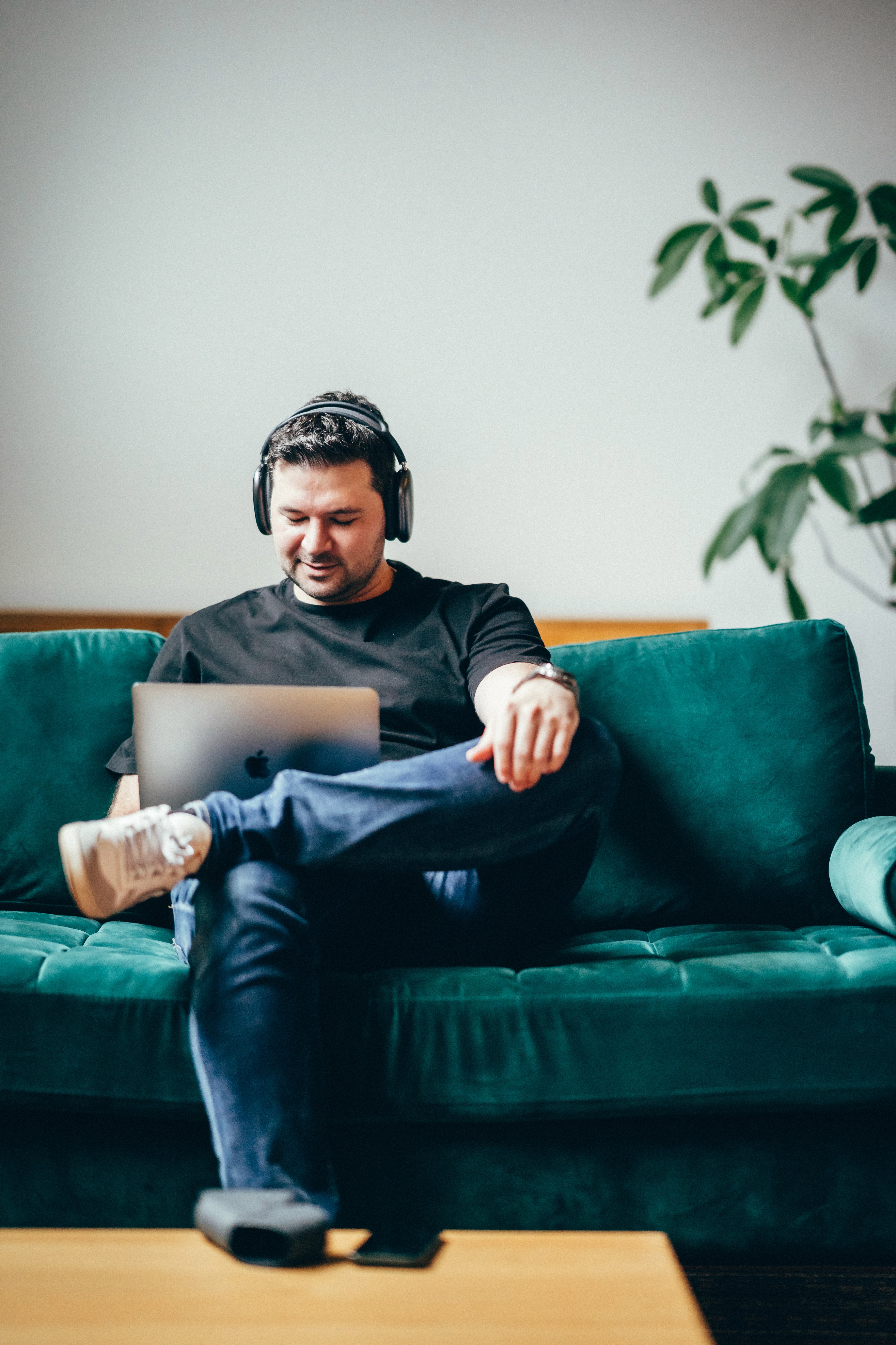 adnan sitzend auf der couch am arbeiten mit Laptop und Overear headphones