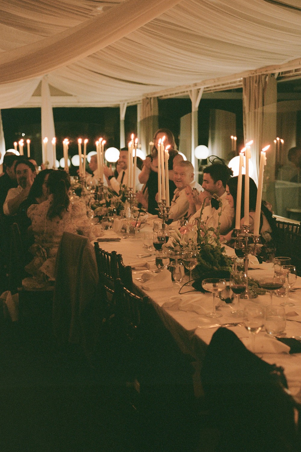 Moody reception scene with candlelight and guests seated at a long wedding table