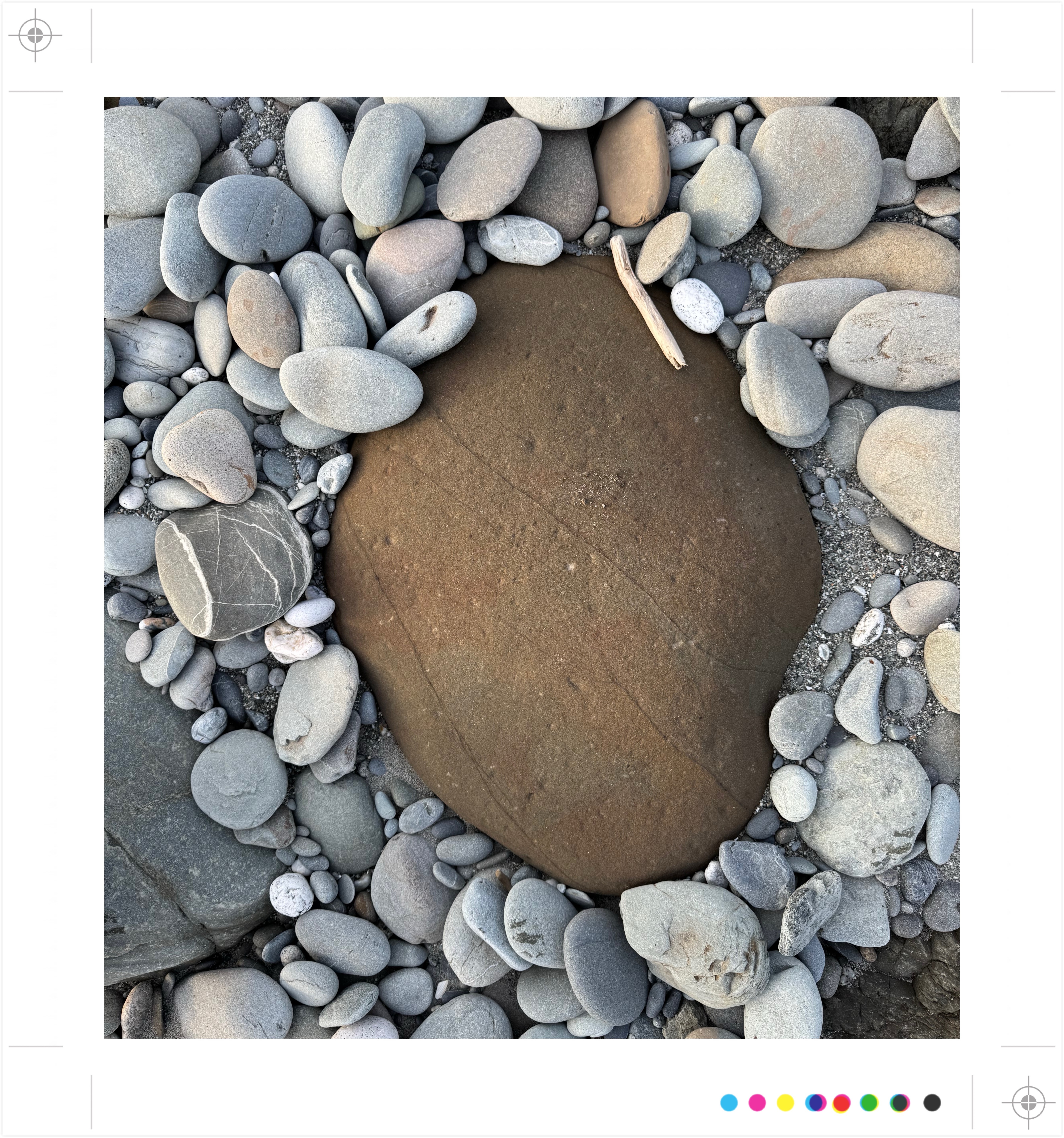 Grote bruine steen omringd door kleinere grijze stenen, met stukje drijfhout.