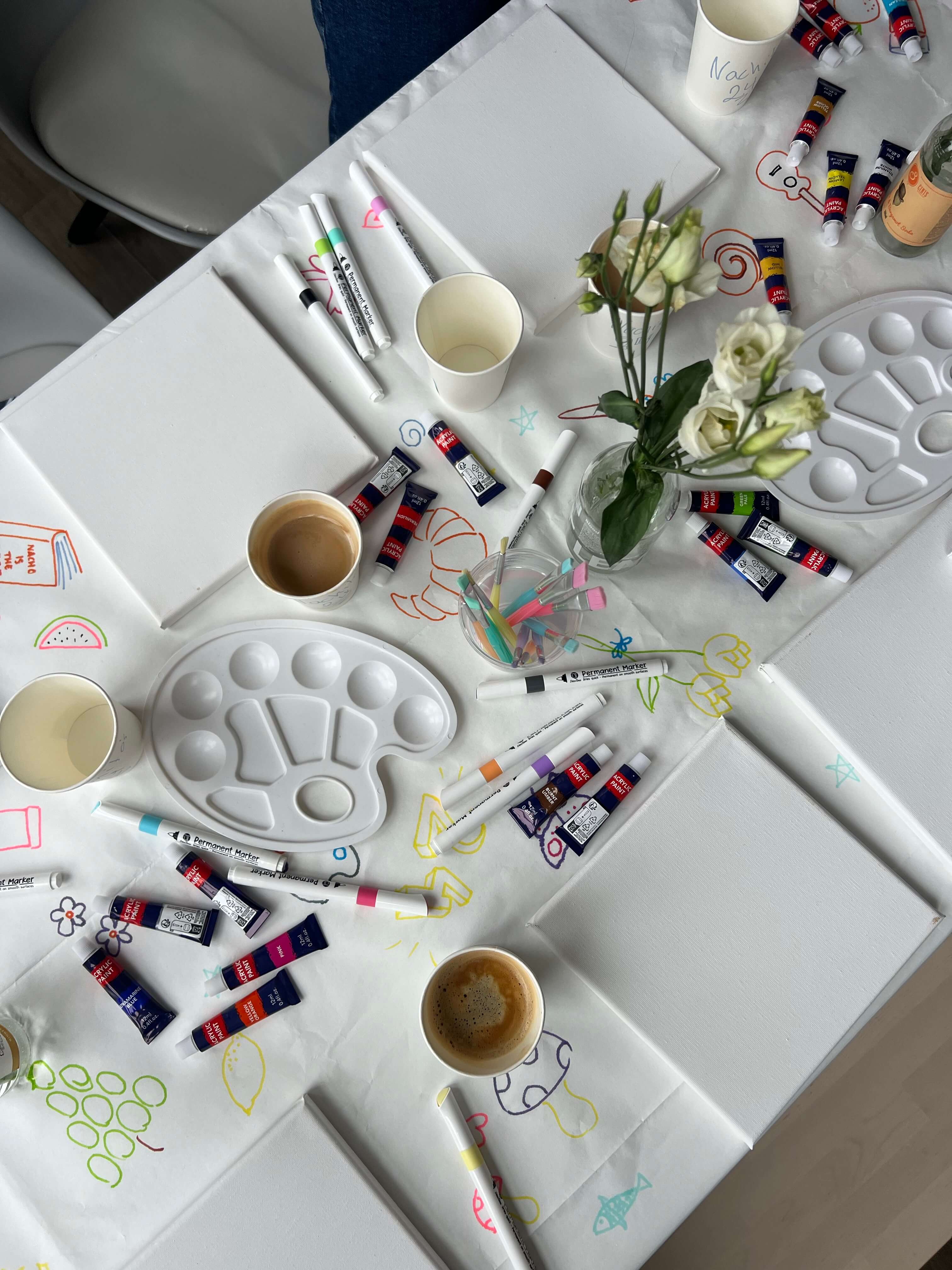 A table set with canvasesb, paint palettes, brushes, and paints