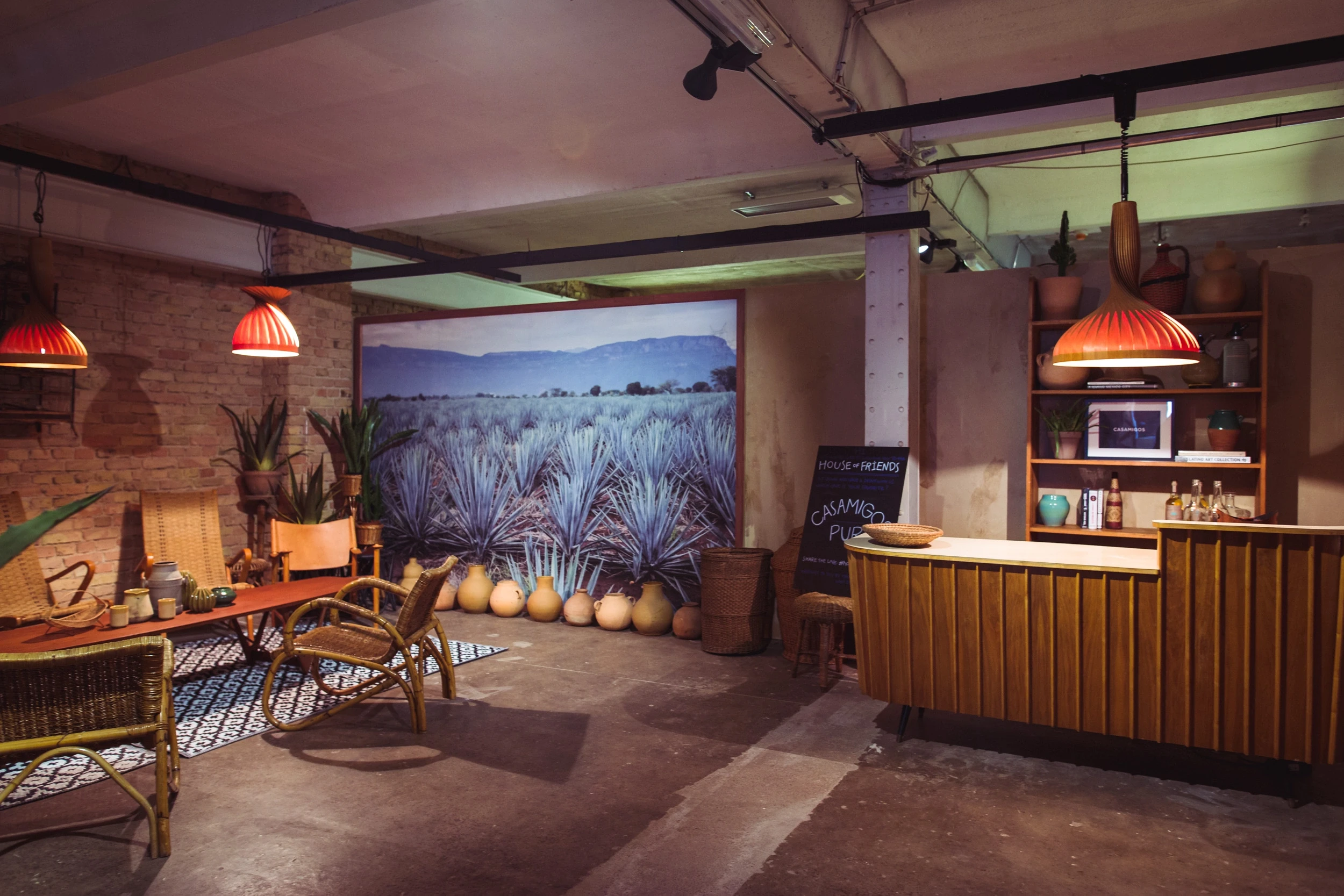Tequila lounge at DIAGEO BCB18 with rattan furniture, a large agave field photo wall, clay jugs and a wooden slat bar with pleated pendant lamps.