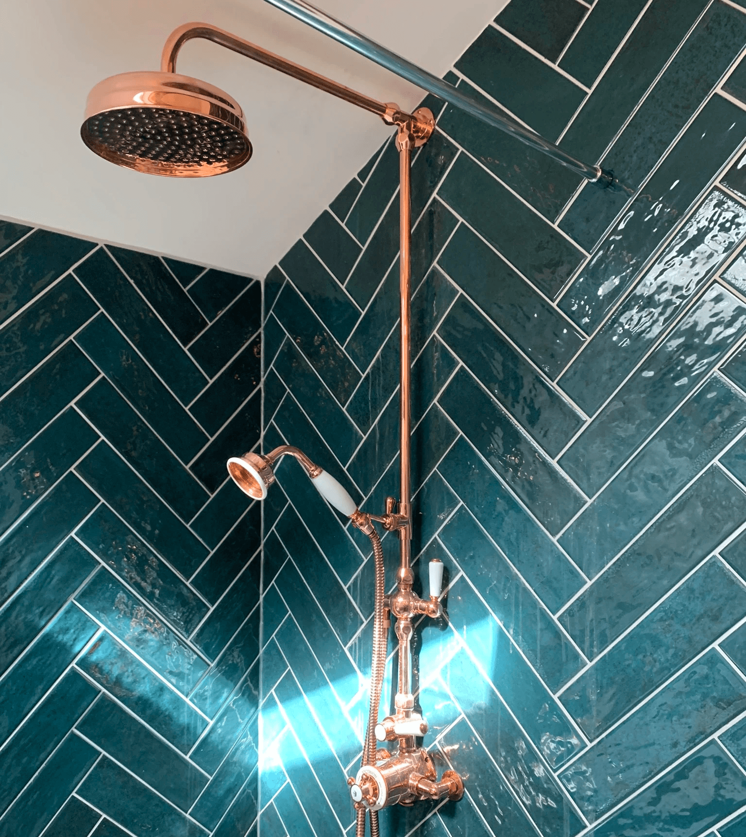 Copper shower fittings in green herringbone tile shower enclosure