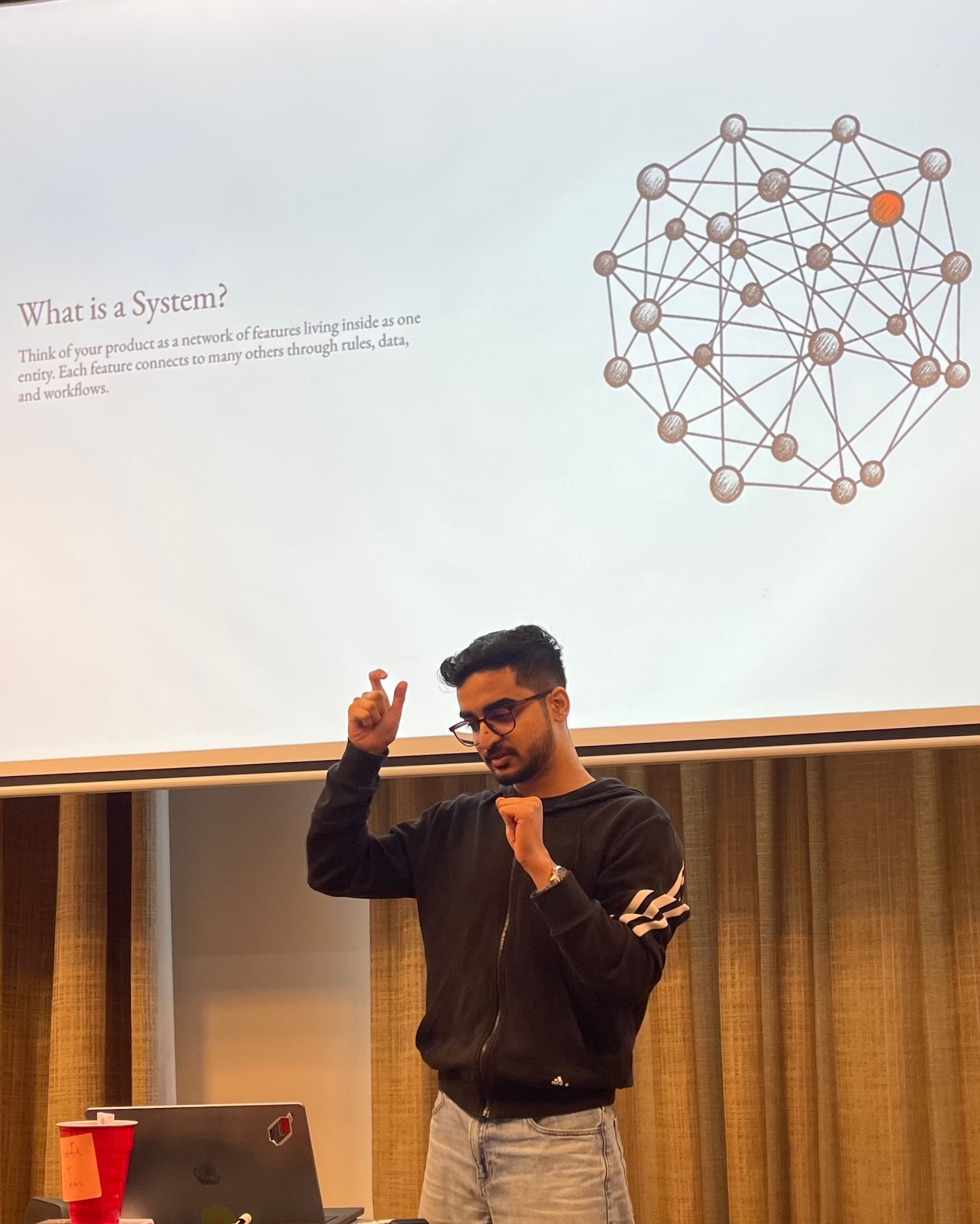 Una persona con una camiseta negra y pantalones de color claro está de pie en la cima rocosa de una montaña al atardecer, sosteniendo una cámara frente a su cara para tomar una foto. Un mar de nubes se extiende detrás de ellos, iluminado por la luz dorada del sol poniente.