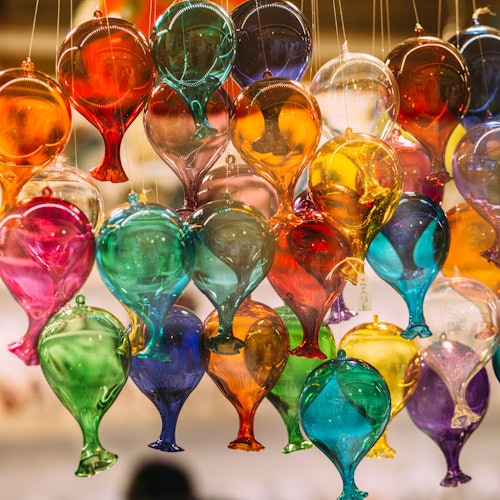 Colorful glass balloons hang in a cluster, each in vibrant shades like red, blue, green, and yellow, against a blurred background.