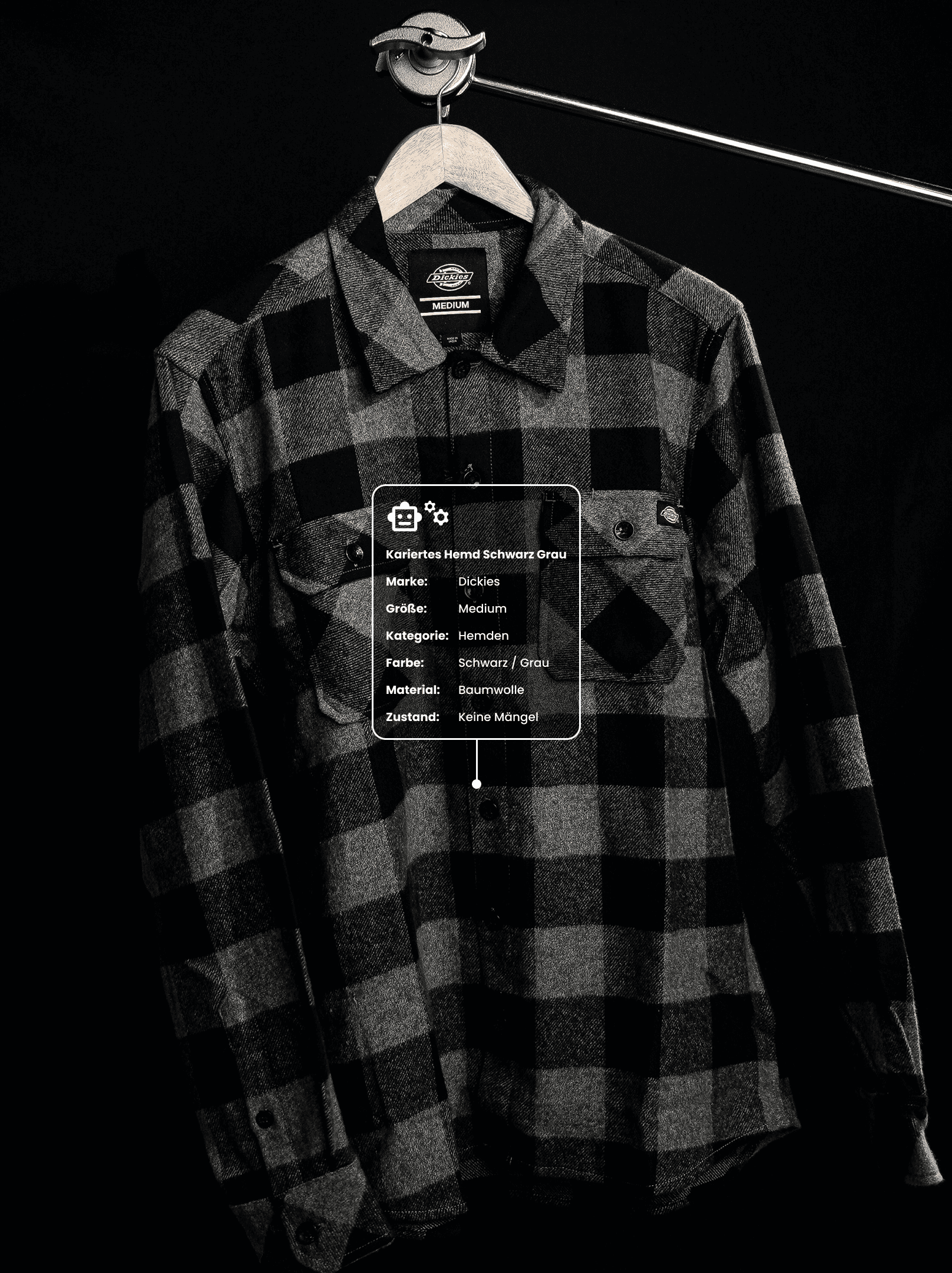 A young person with curly hair smiles at the camera while sitting in front of a laptop against a dark background.