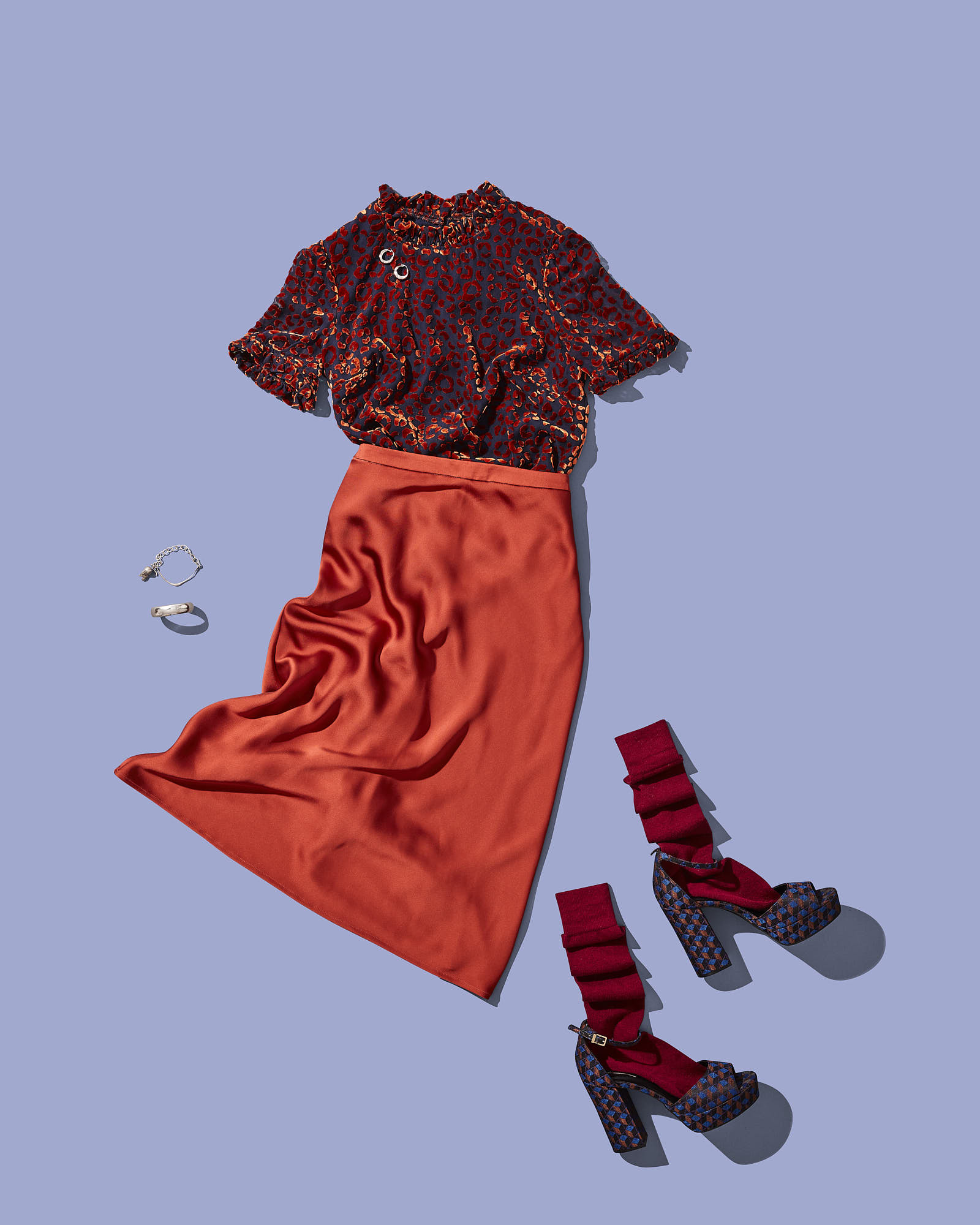 Stylish outfit with red floral blouse, matching orange skirt, red socks, high heels, and accessories on blue background.