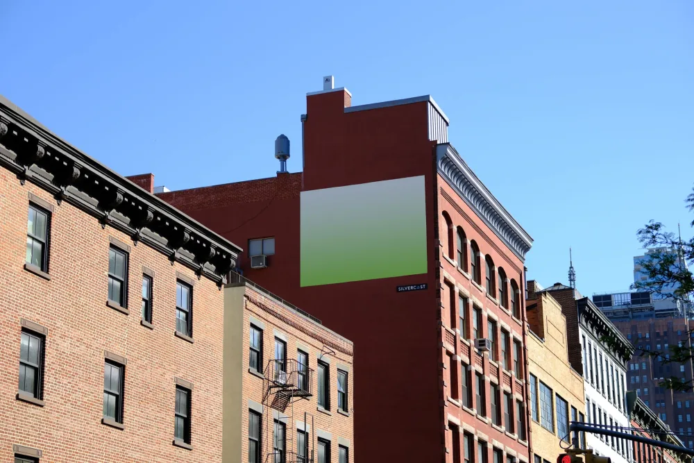 Large billboard mockup displayed on a red brick building in an urban setting. The billboard features a gradient design, surrounded by classic architectural details and a clear blue sky.