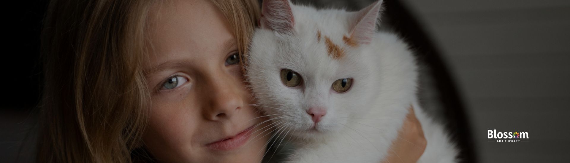 Young child gently holding a white cat indoors.