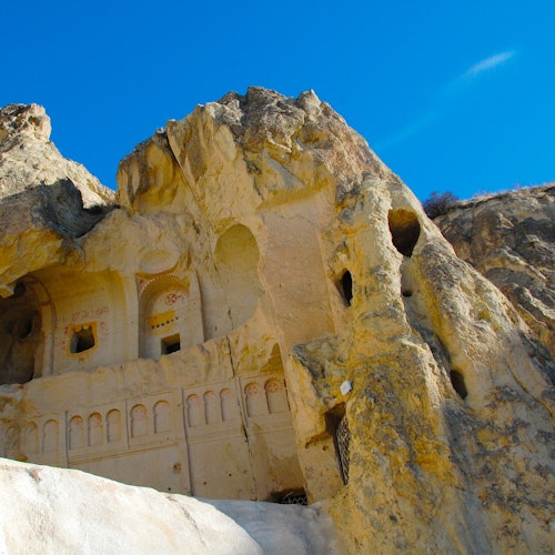 Ancient rock-cut architecture carved into a rocky cliff under a clear blue sky.