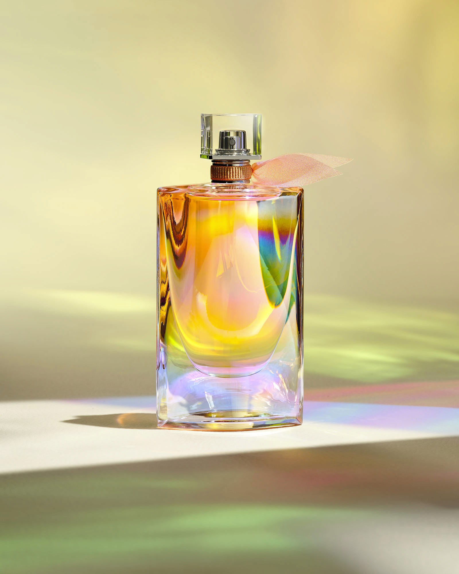 A colorful, stylized perfume bottles stands on a smooth surface with a soft, blurred background in pastel hues.