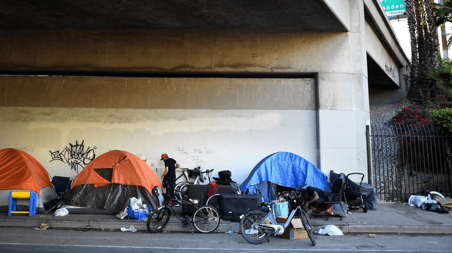 Three tents under a bridge among trash. 