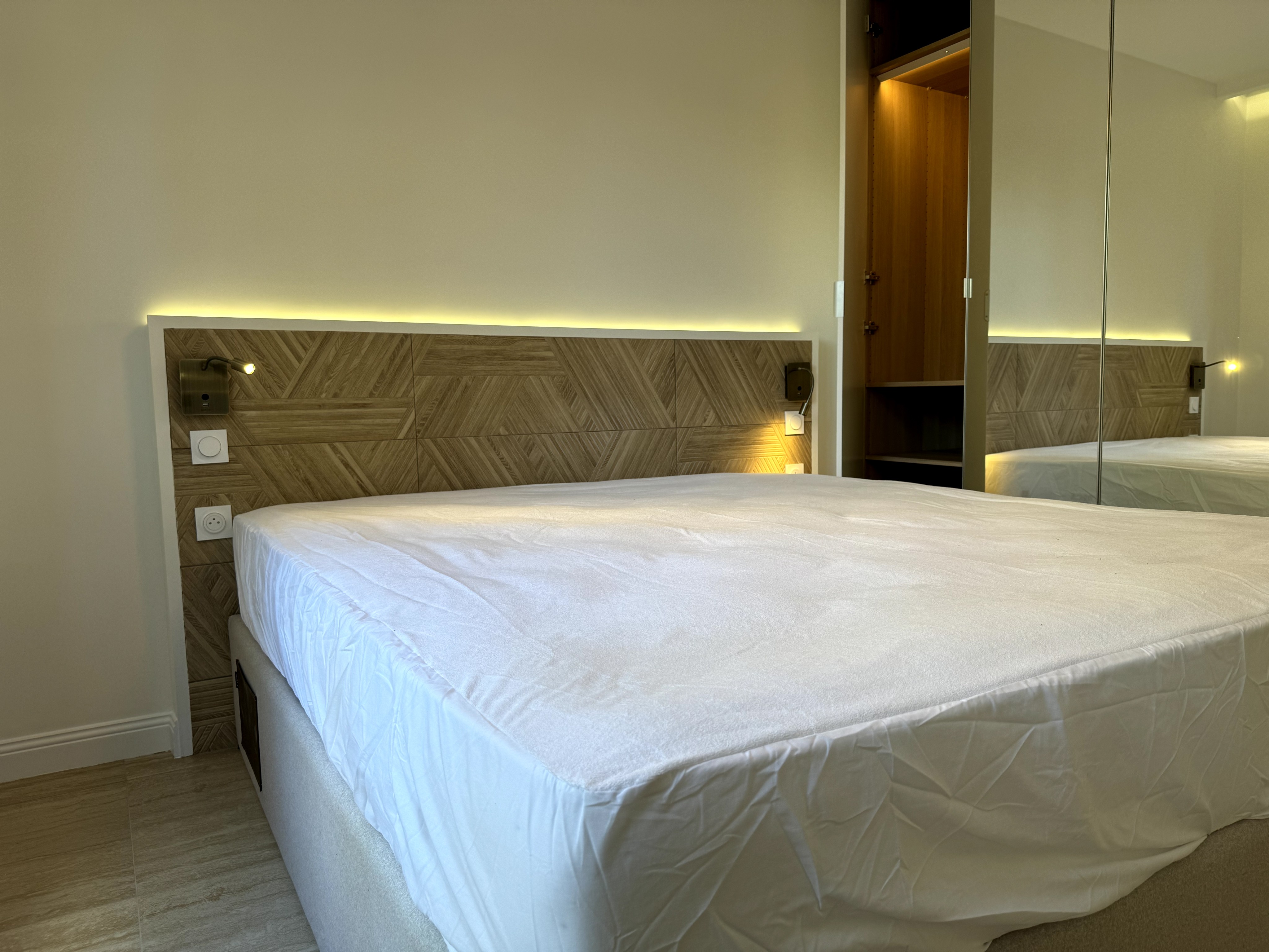 Tête de lit architecturale en pierre texturée avec éclairage indirect et liseuses intégrées.