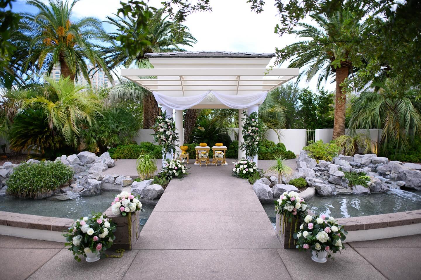 Outdoor restaurant terrace overlooking a tranquil lake at sunset. White tables and chairs are set with glassware. Sheer curtains add elegance. Calm ambiance.