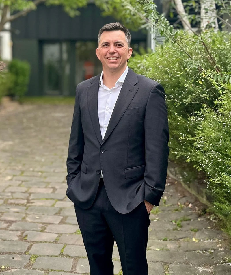 A profile photo of Andrew Humphries in a suit in a leafy outdoor setting