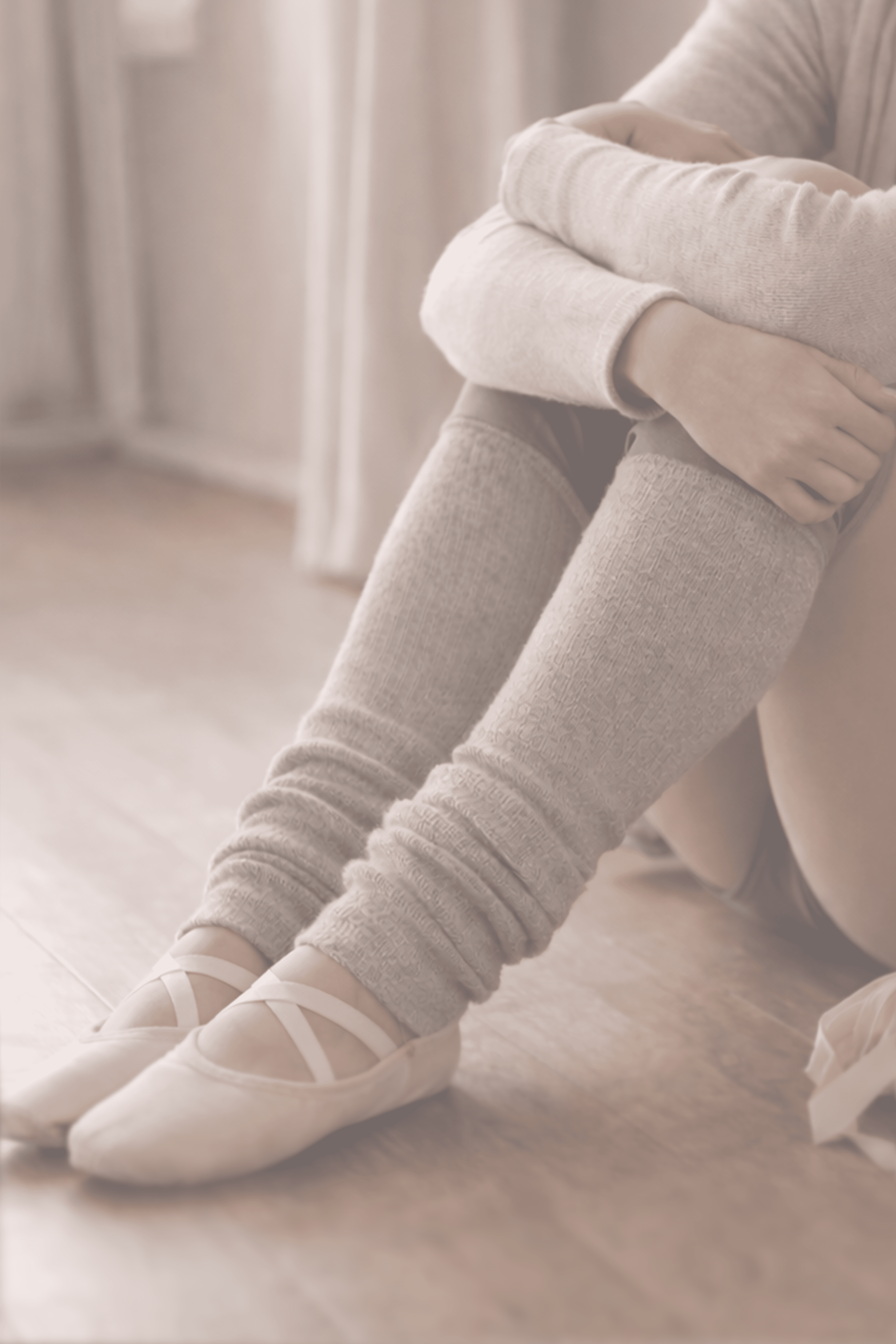 Adult ballet dancer sitting on the floor wearing leg warmers and ballet slippers