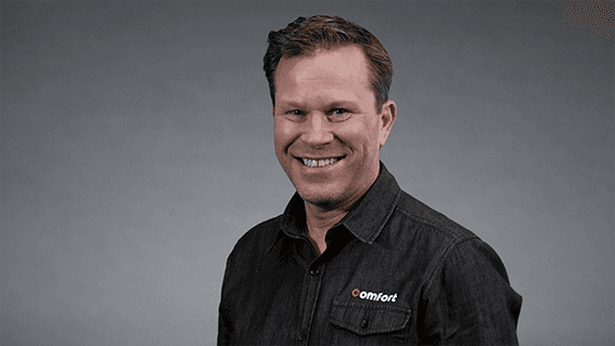 Vidar Skoglund kjededirektør i Comfort i sort skjorte med Comfort logo foran nøytral grå bakgrunn