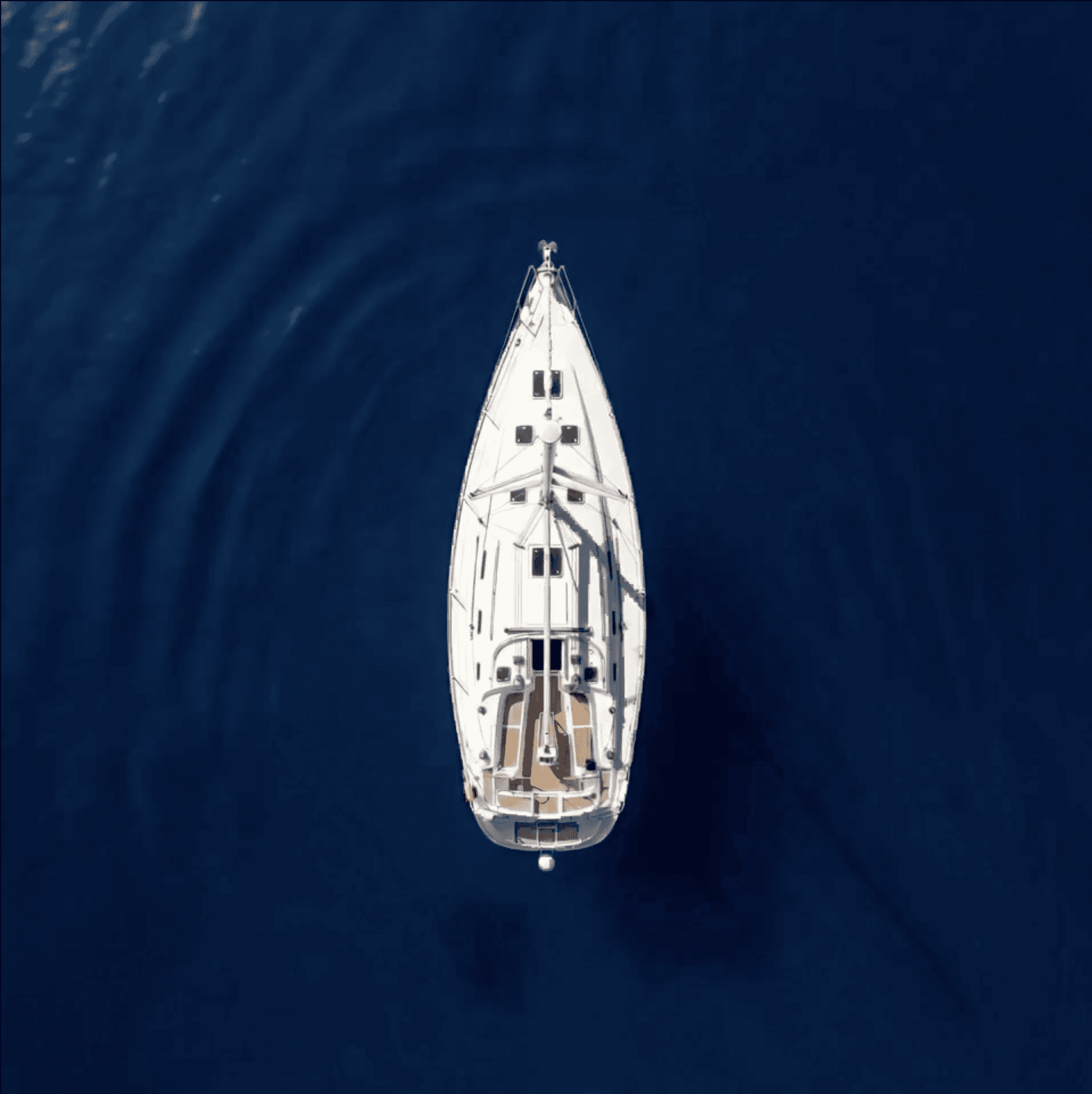 Overhead night aerial photograph of a Beneteau Clipper 361 sailing yacht with warm interior cabin lighting illuminating the teak deck, set against a dark black ocean background