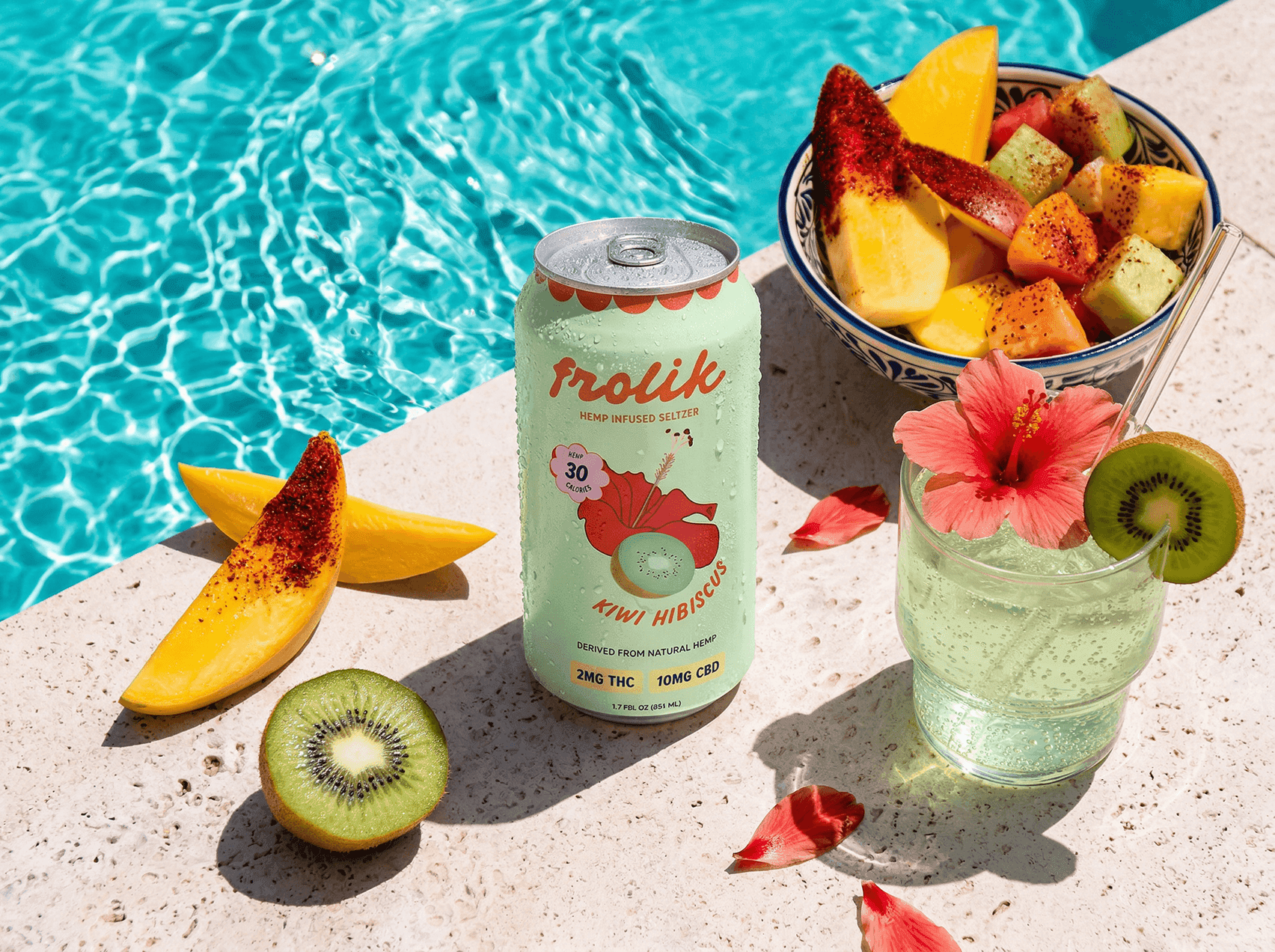 Frolik seltzer can by the pool surrounded by cut fruit and a fruit bowl.