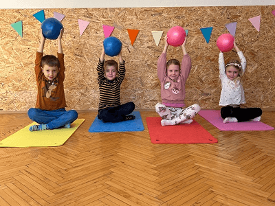 Skupina dívek a chlapců cvičící na podložkách s míči nad hlavou