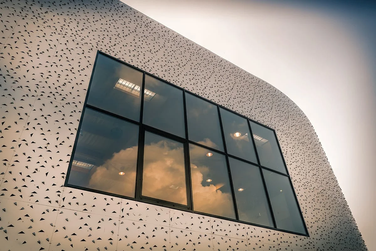 Façade perforée blanche avec grande baie vitrée reflétant le ciel — architecture contemporaine à seclin