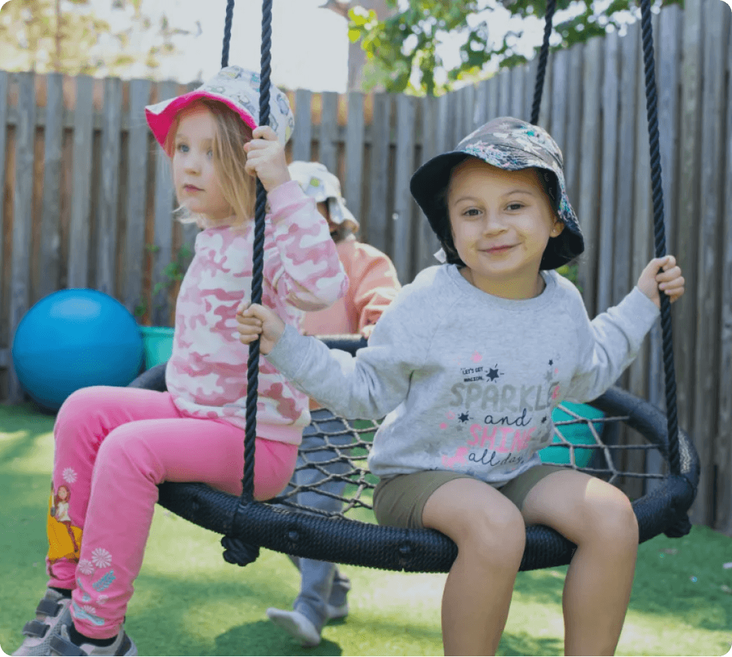Children playing together on an outdoor swing at Kaleidoscope Kids childcare centre in Brisbane.