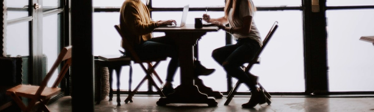 Two people seated across a table against a wall of glass