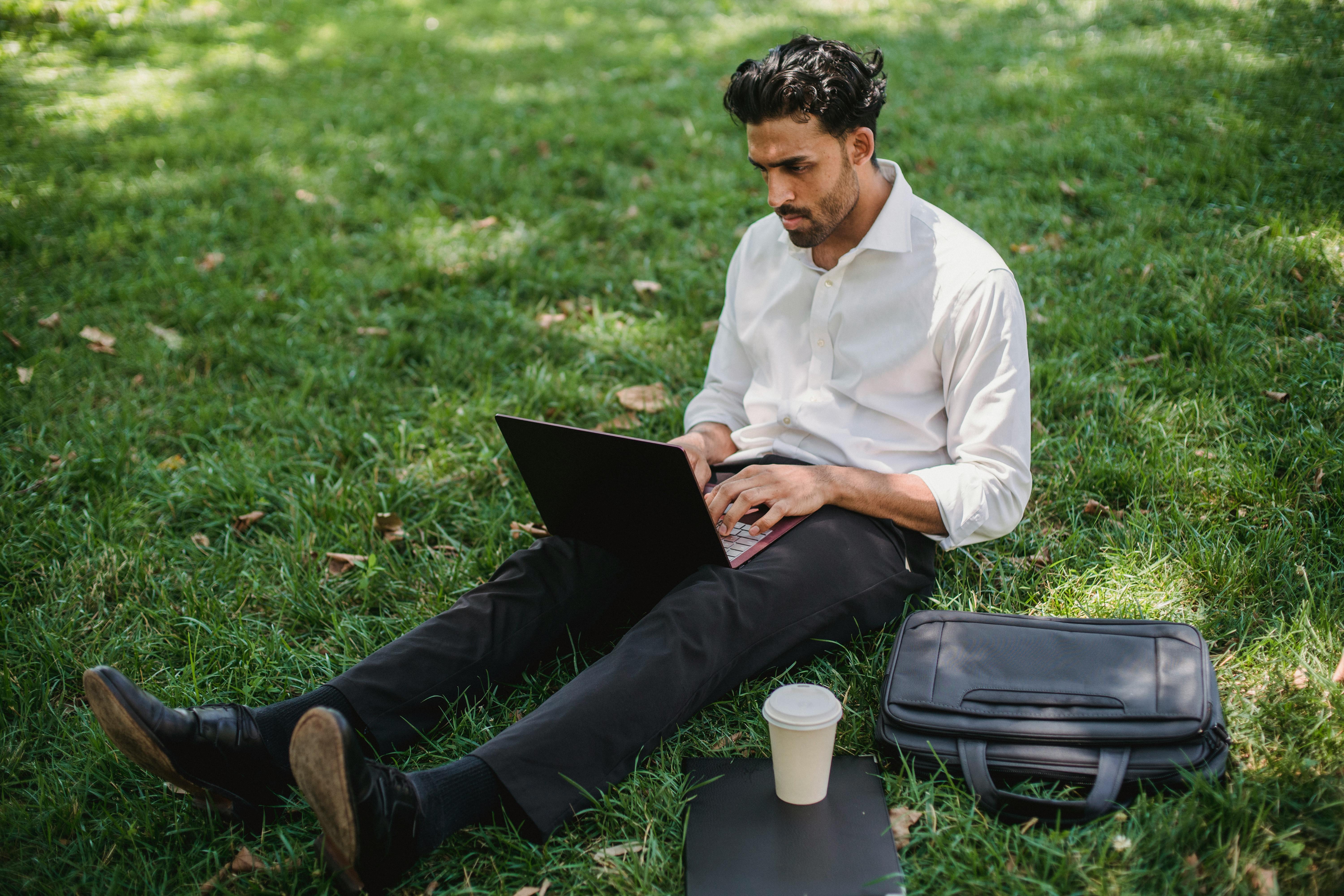 Businessman sitting on grass studying cold emails