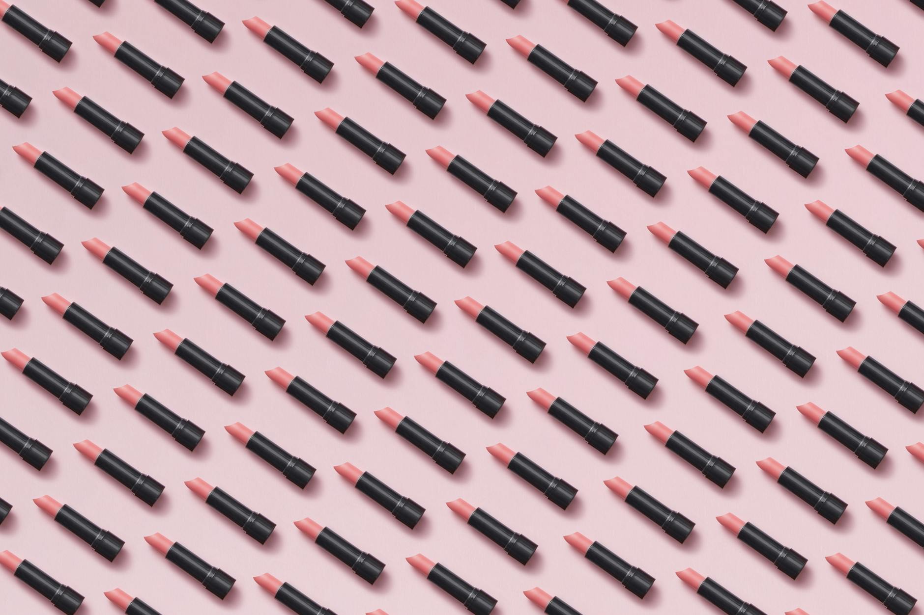 Flat lay of pink lipsticks arranged in a geometric pattern on pastel background.