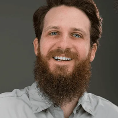 Close up portrait of a smiling man with a full beard and blue eyes wearing a light gray shirt.
