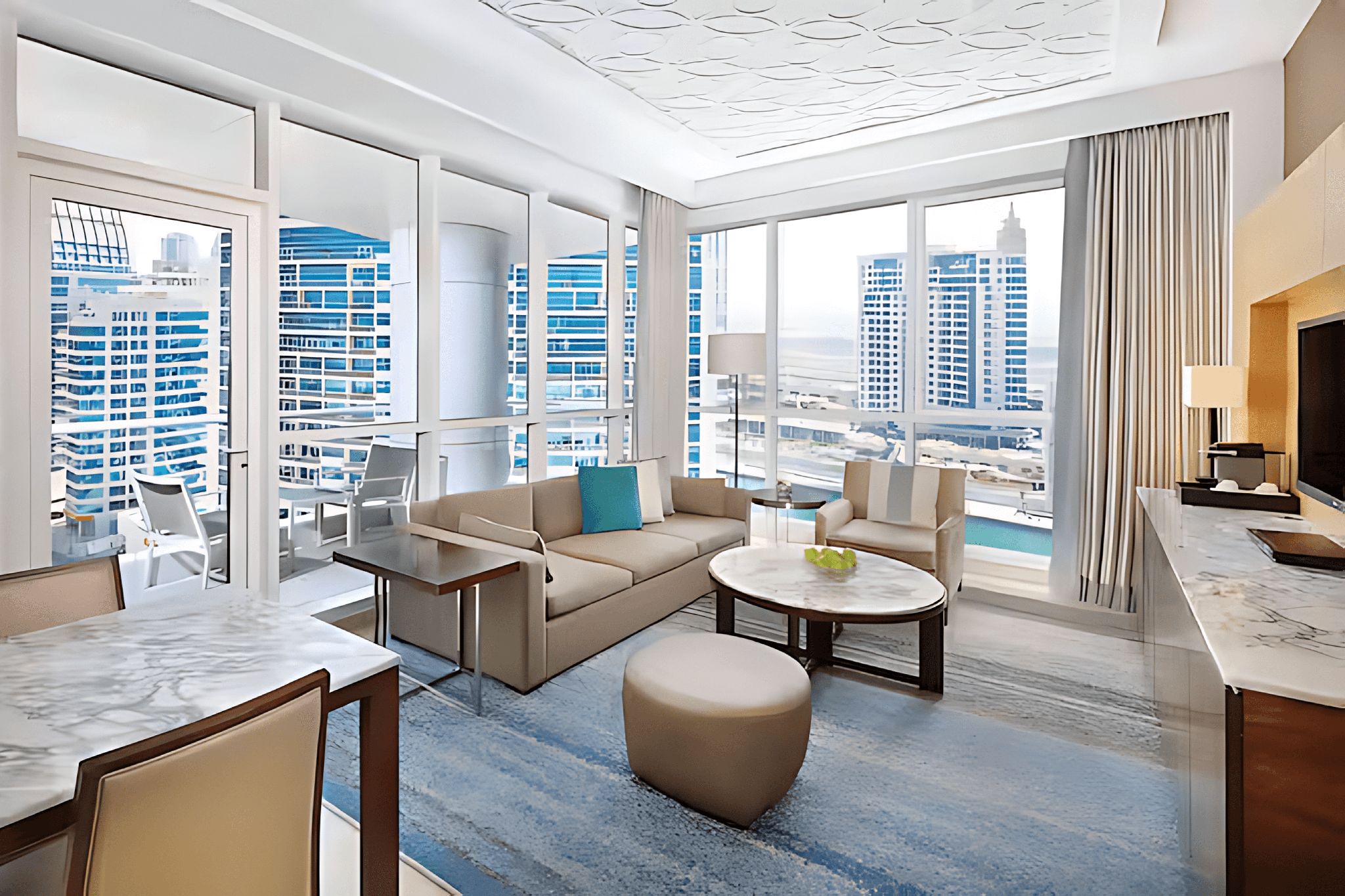 A compact hotel room featuring comfortable seating, an outdoor balcony, and a dining set.