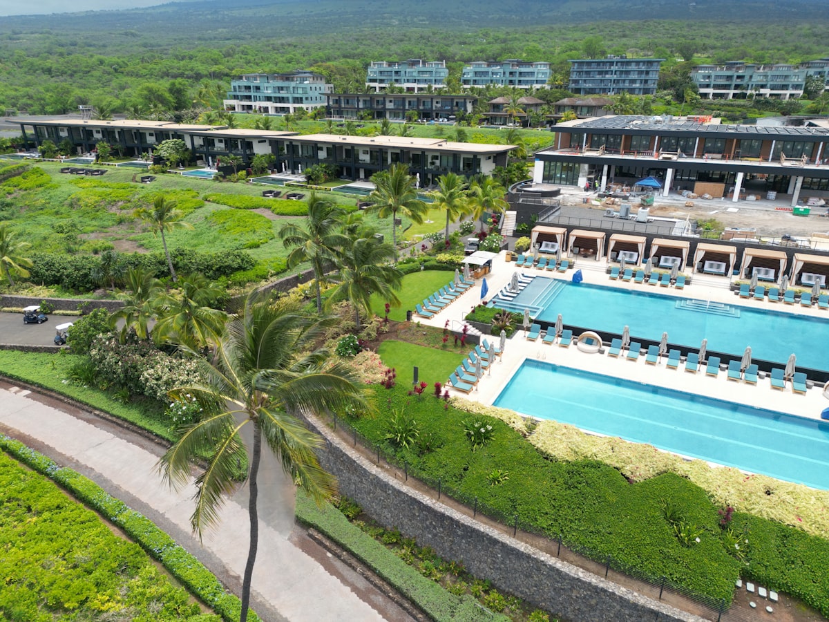 Tropical resort with two swimming pools, palm trees and mountains behind, where Hawaii resort fees get charged