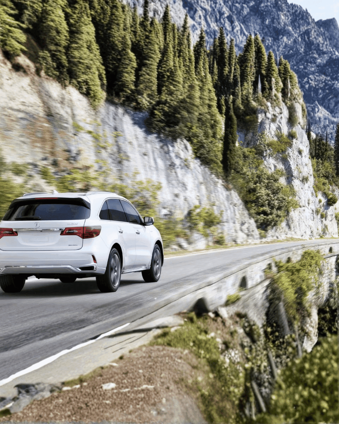 White Acura MDX driving on a scenic mountain road.