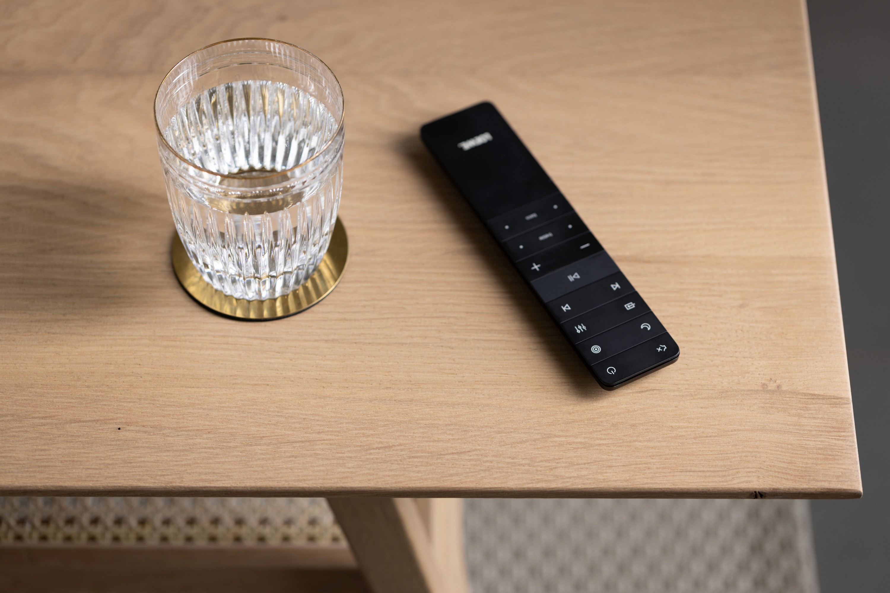 een whiskeyglas en de afstandbediening van een televisie liggen op een eikenhouten tafelblad van een koffietafel