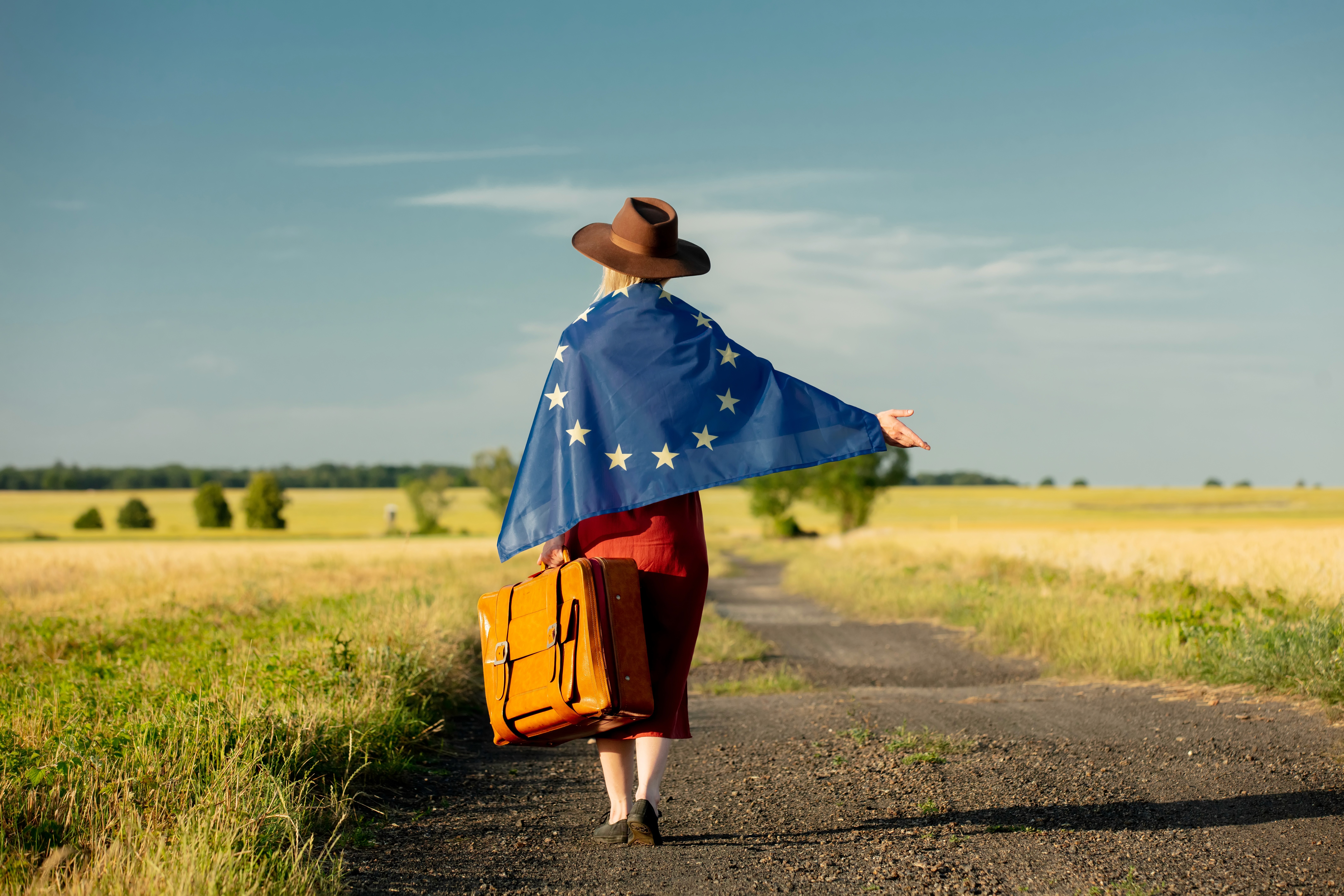 Vrouw met koffer gewikkeld in EU-vlag, symbool voor emigratie binnen Europa en vrijheid van reizen.
