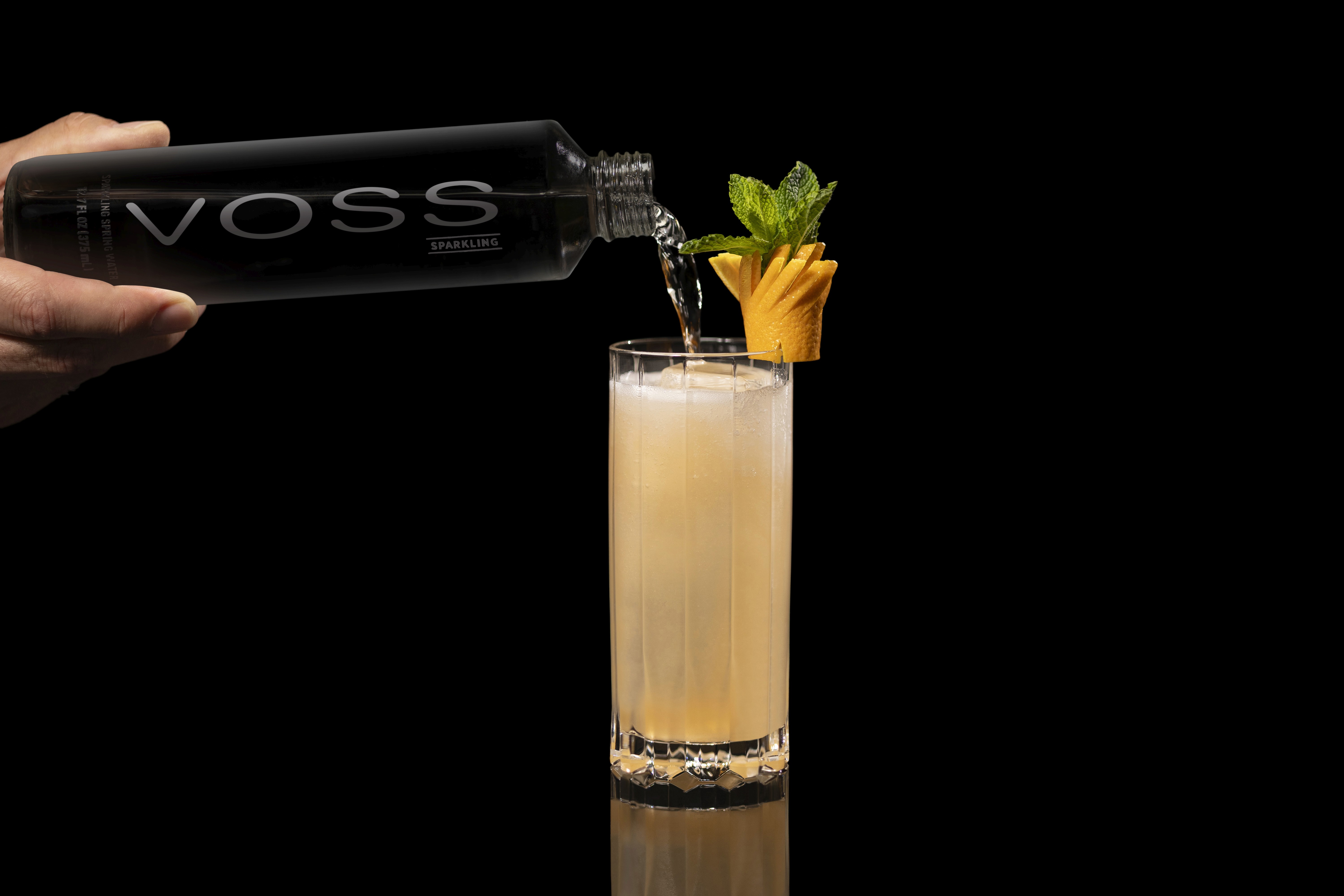 A bottle of Voss being poured into a glass of Miami Spritz on a bar counter.