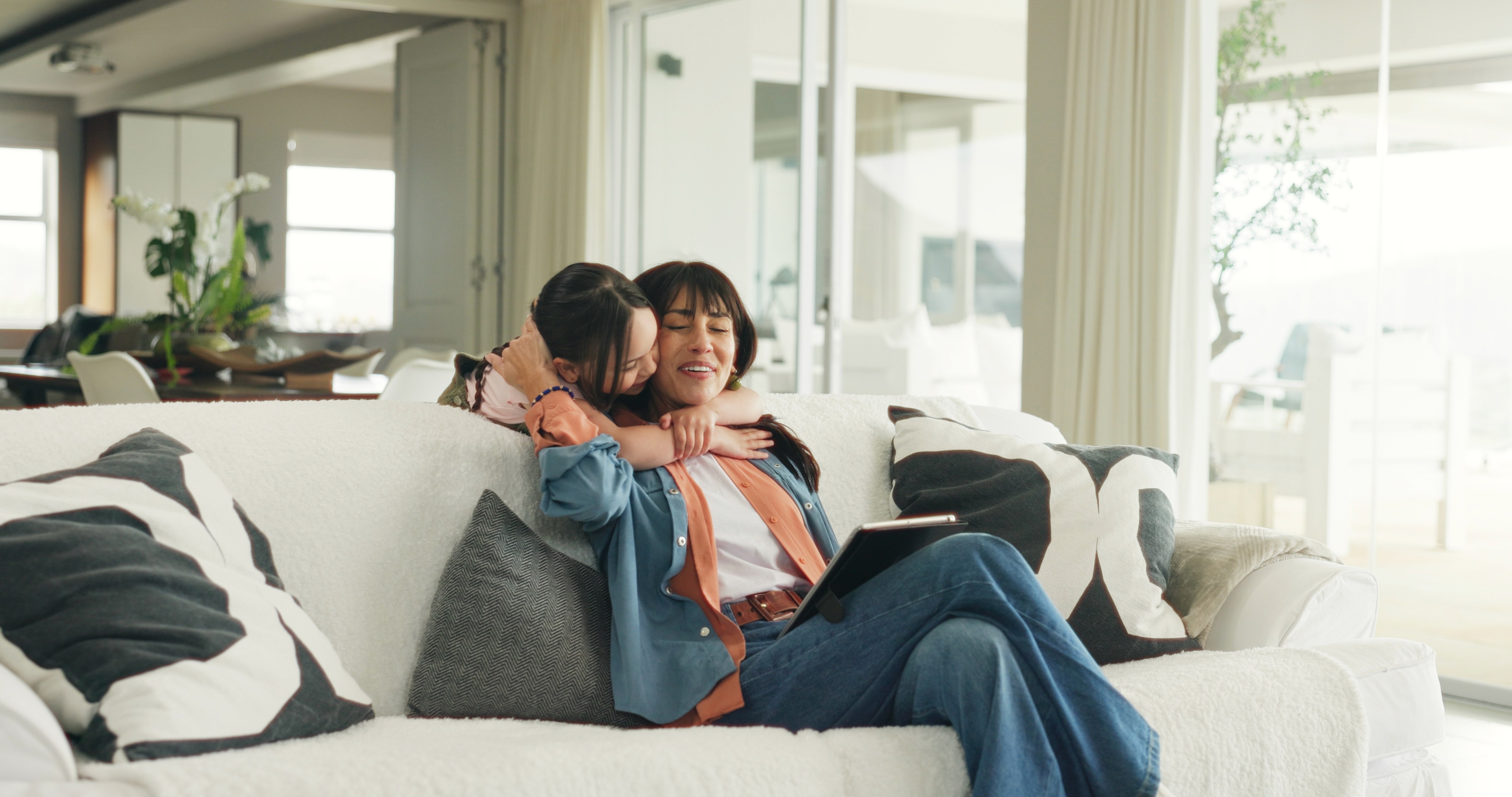 A smiling man with a beard wearing a dark green shirt, sitting at a table with a notebook, coffee cup, and laptop. He gestures with one hand while speaking, with a colorful abstract artwork framed behind him.