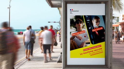 Affiche publicitaire du gouvernement français pour le recrutement dans le secteur du tourisme, placée dans un abribus en bord de mer. L'affiche clame "Le tourisme recrute" et montre des photos de métiers du secteur.